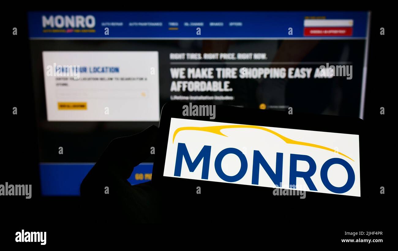 Personne tenant un téléphone portable avec le logo de la société de service automobile américaine Monro Inc. À l'écran devant la page Web d'affaires. Mise au point sur l'affichage du téléphone. Banque D'Images