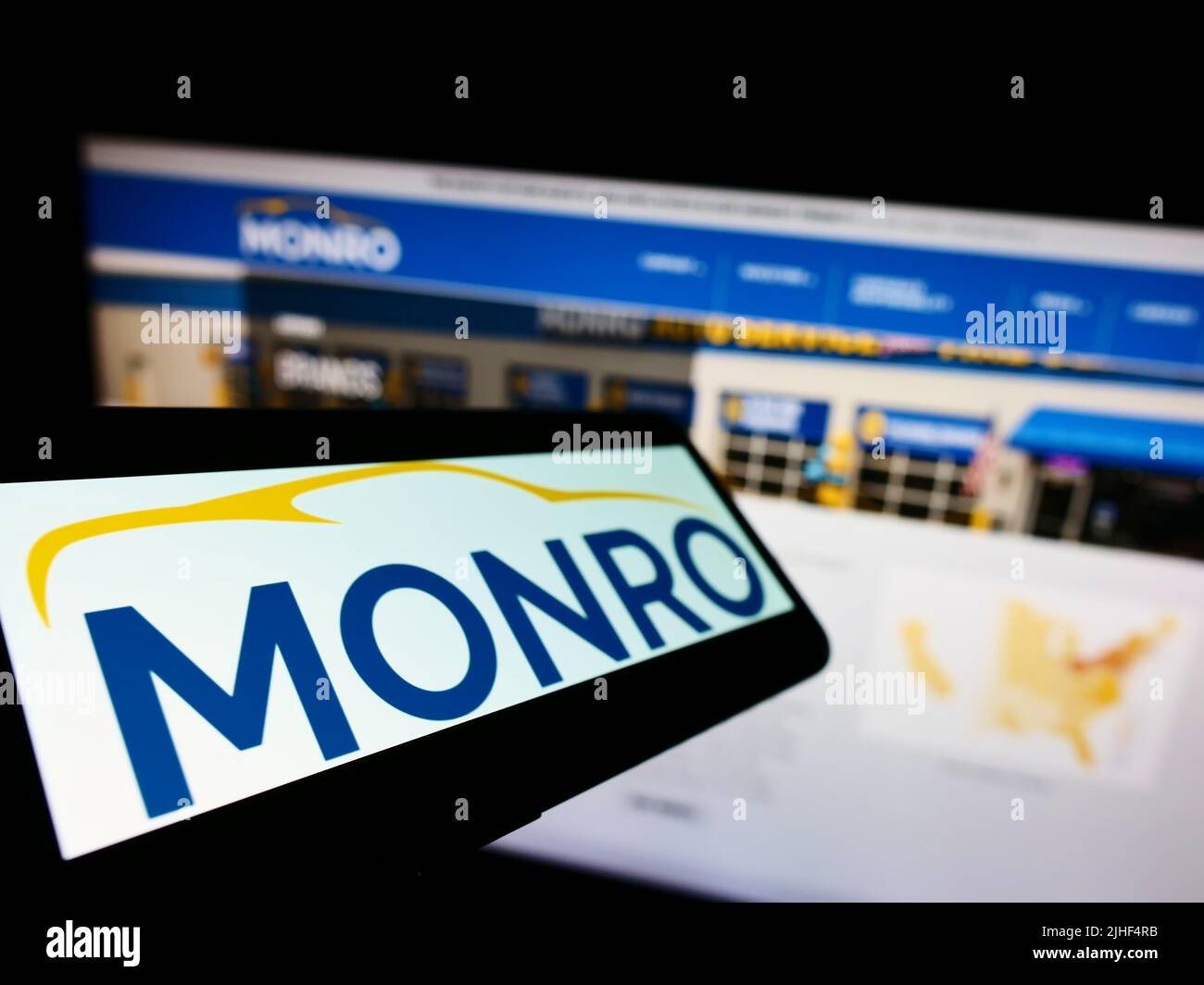 Téléphone portable avec logo de la société américaine de service automobile Monro Inc. À l'écran en face du site Web d'affaires. Mise au point à gauche de l'écran du téléphone. Banque D'Images
