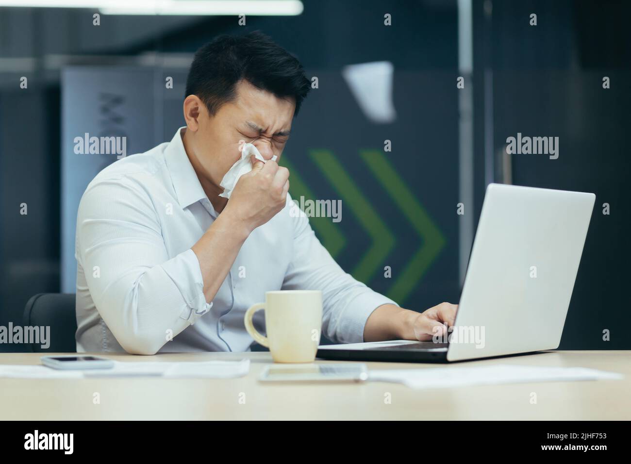 Malade dans le bureau tousse et a le nez qui coule, homme d'affaires asiatique avec froid travaille dans le bureau sur ordinateur portable Banque D'Images