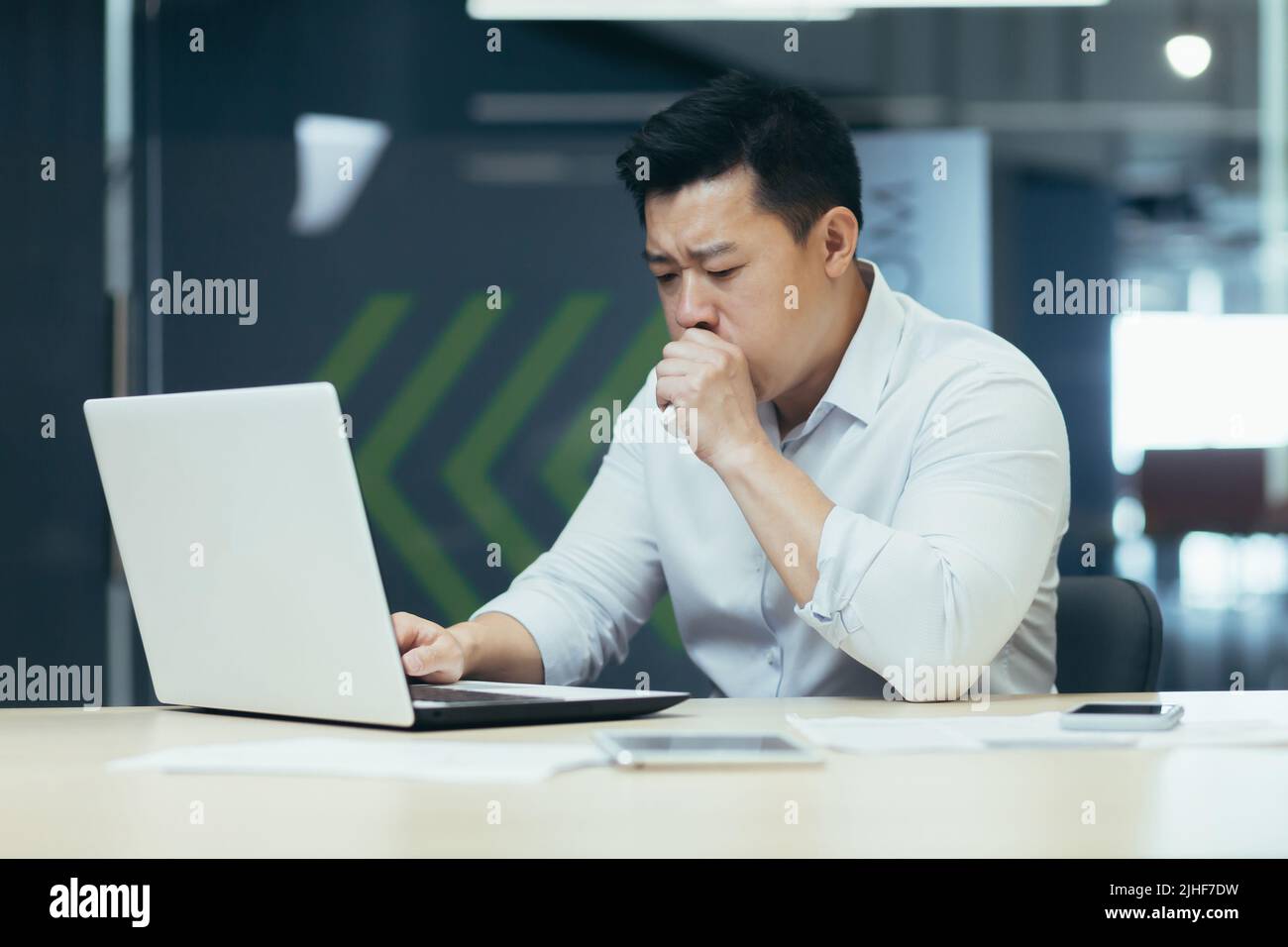 Malade dans le bureau tousse et a le nez qui coule, homme d'affaires asiatique avec froid travaille dans le bureau sur ordinateur portable Banque D'Images