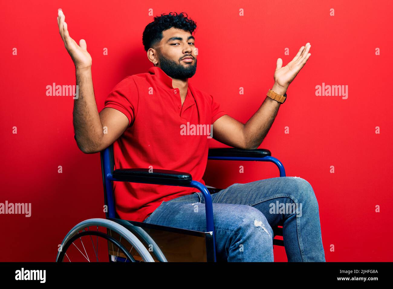 Homme arabe avec barbe assis sur un fauteuil roulant expression sans indice et confuse avec les bras et les mains soulevées. Doute concept. Banque D'Images