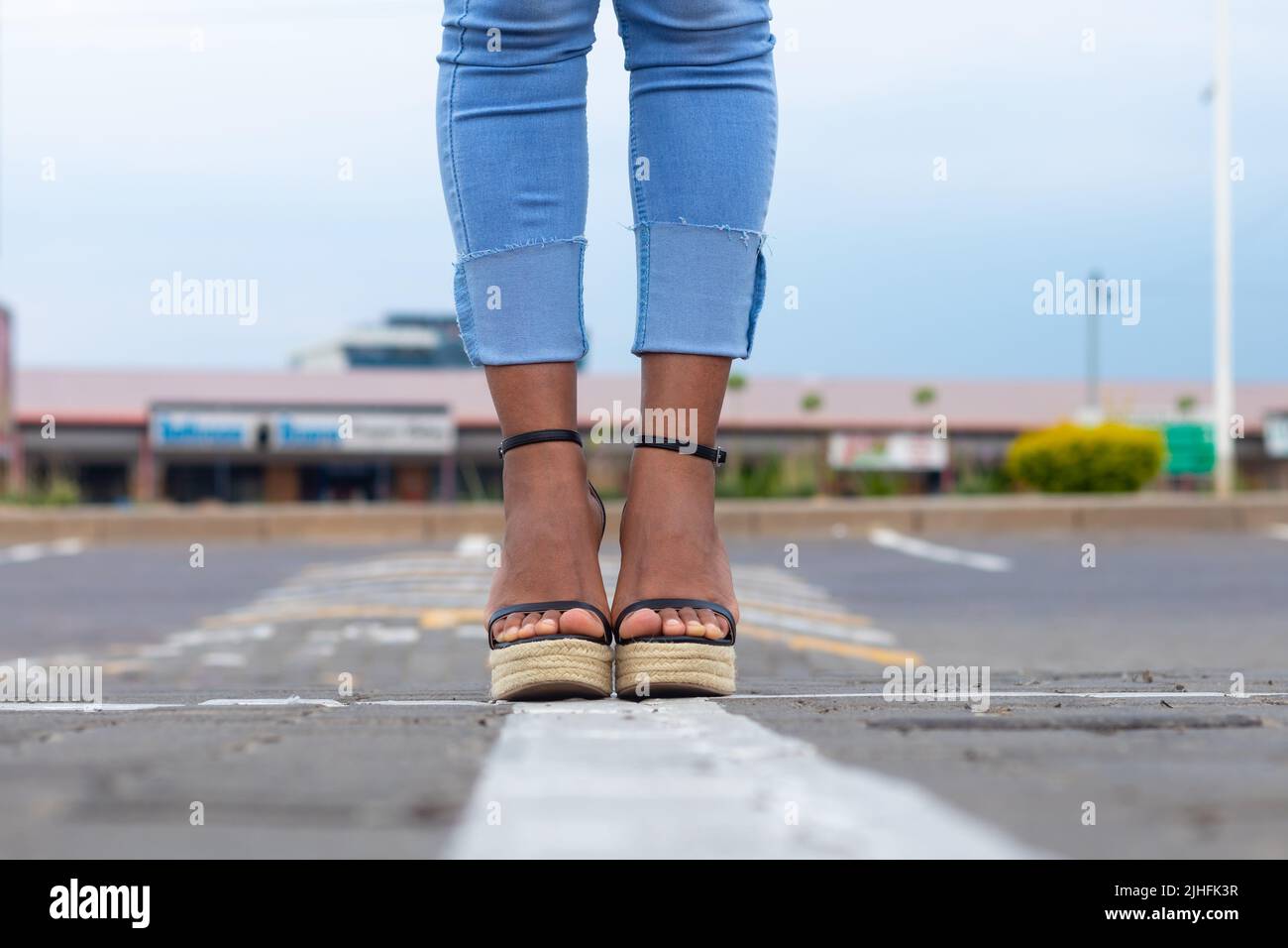 Femme en Jean bleu élégant et sandales compensées debout dans une rue urbaine. Banque D'Images