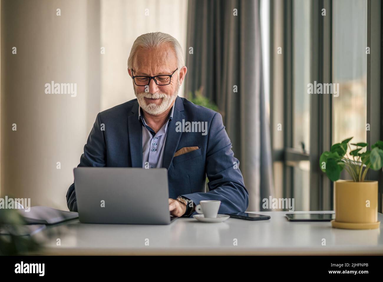 Homme d'affaires expérimenté confiant travaillant sur un ordinateur portable. Un Manager de sexe masculin âgé portant des lunettes utilise un ordinateur sans fil. Il est en forme en étant assis à Banque D'Images