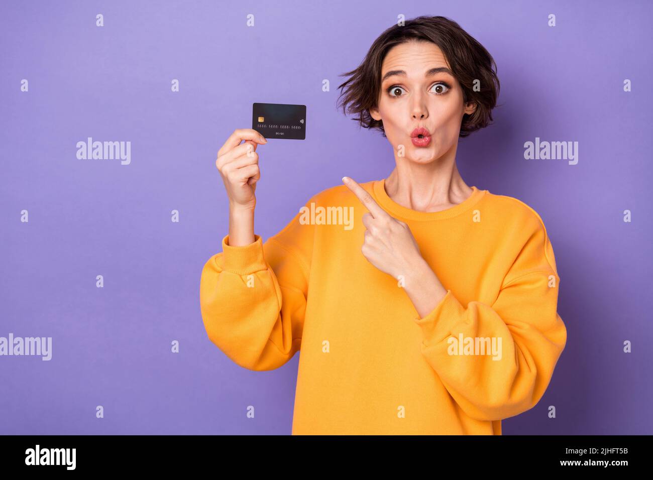 Portrait d'une jolie fille rabouée tenant dans la main démontrant la carte de banque pout lèvres isolées sur fond violet lilas couleur Banque D'Images