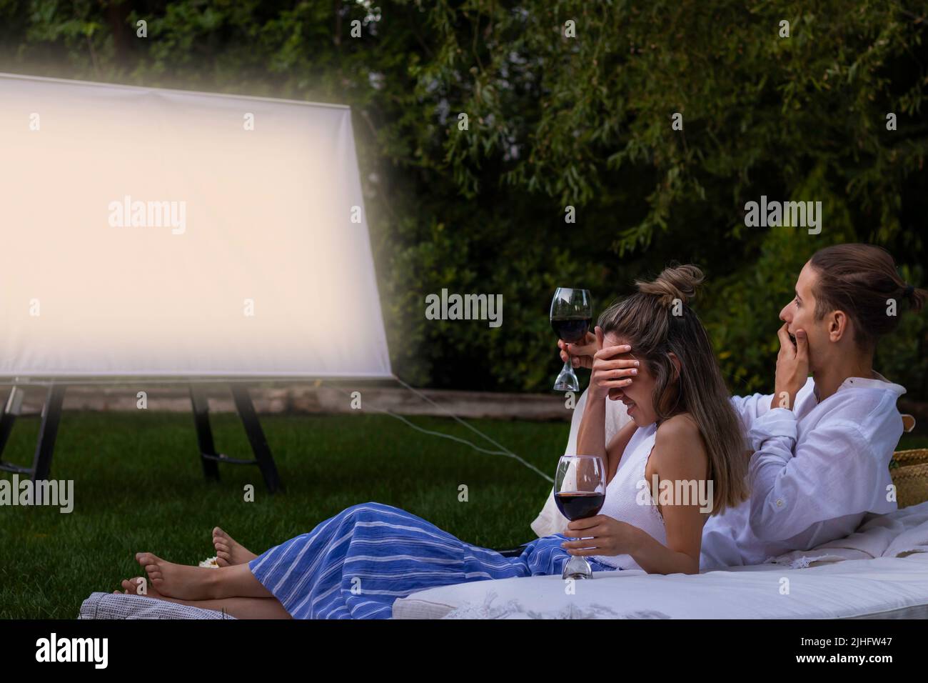 Un jeune couple regardant un film d'horreur dans le parc de la ville la nuit surpris et couvrant ses yeux avec la main Banque D'Images