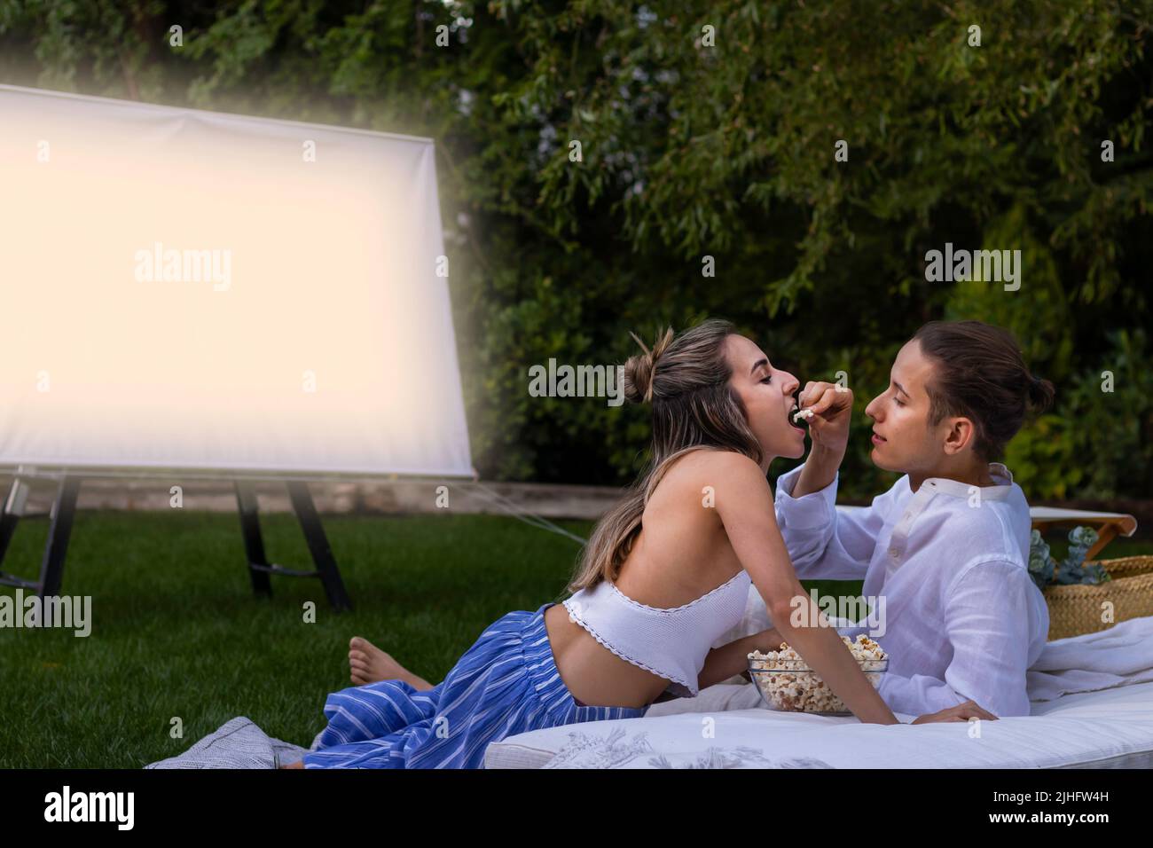 Jeune couple hétérosexuel mangeant des popcorns romantiques comme un signe d'amour dans le cinéma de jardin Banque D'Images