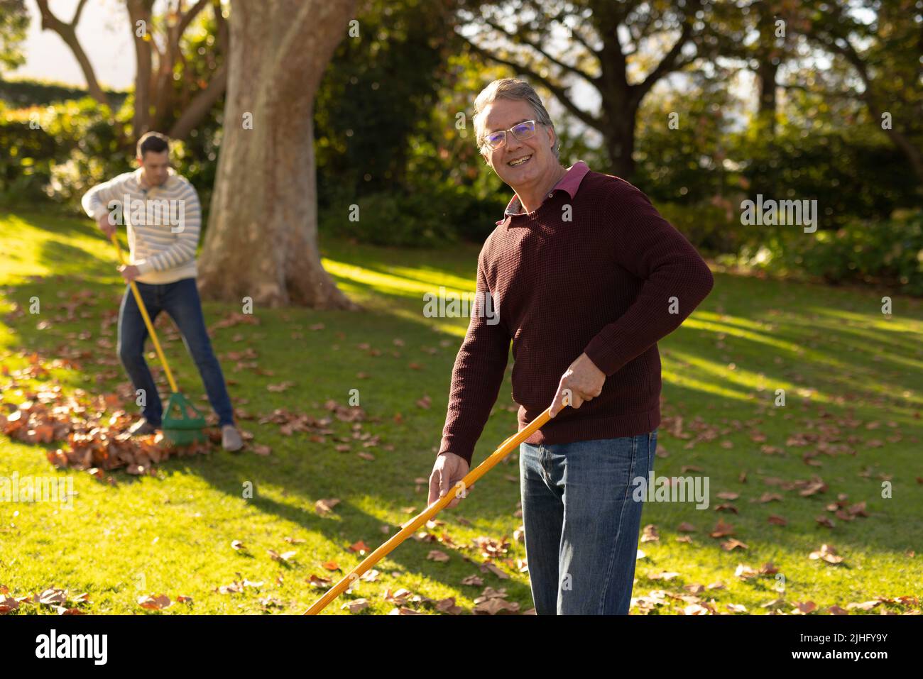 Image d'un père caucasien heureux et d'un fils adulte qui balaie les feuilles dans le jardin Banque D'Images
