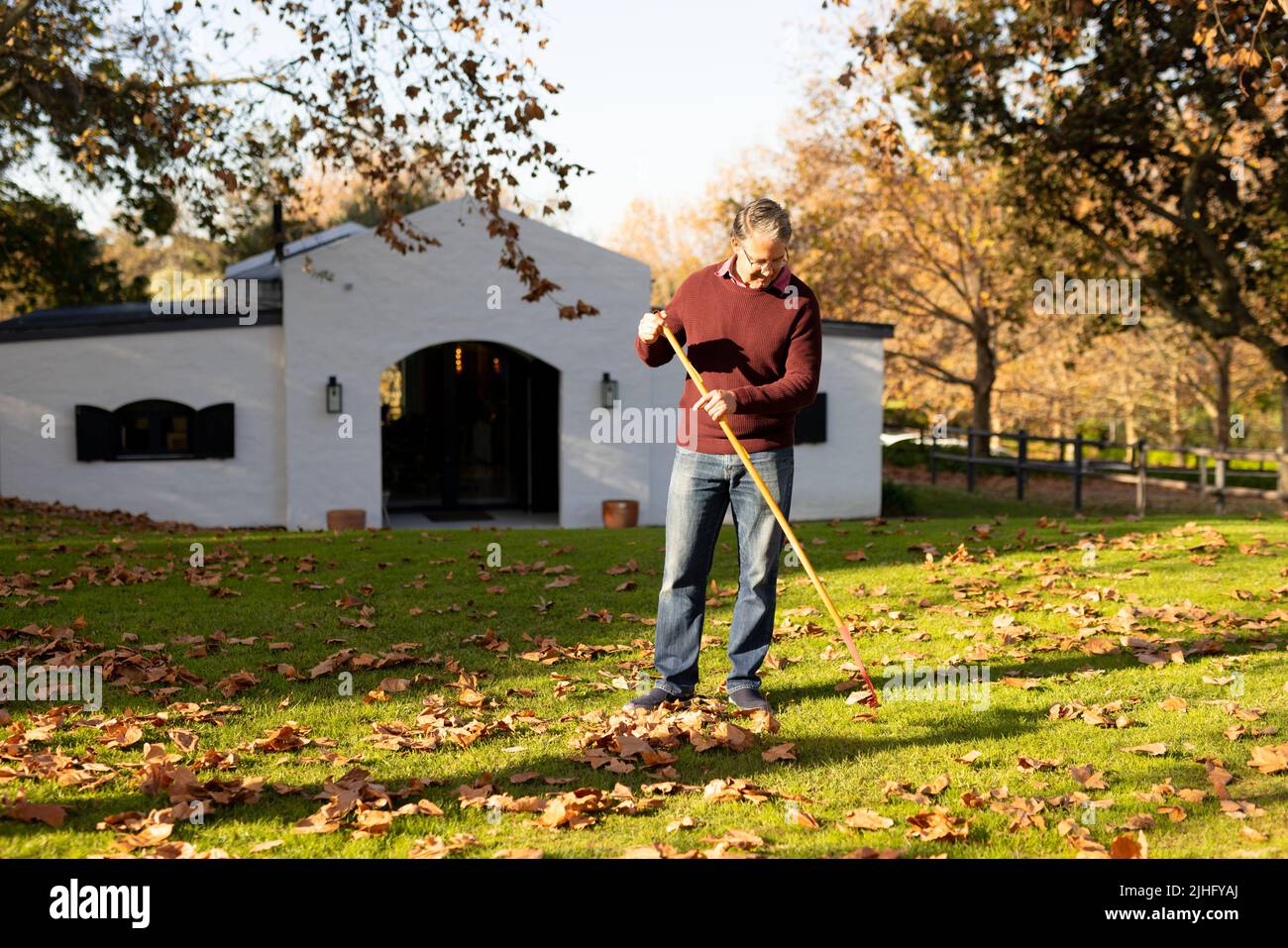 Image d'un homme âgé caucasien heureux qui balaie les feuilles dans le jardin Banque D'Images