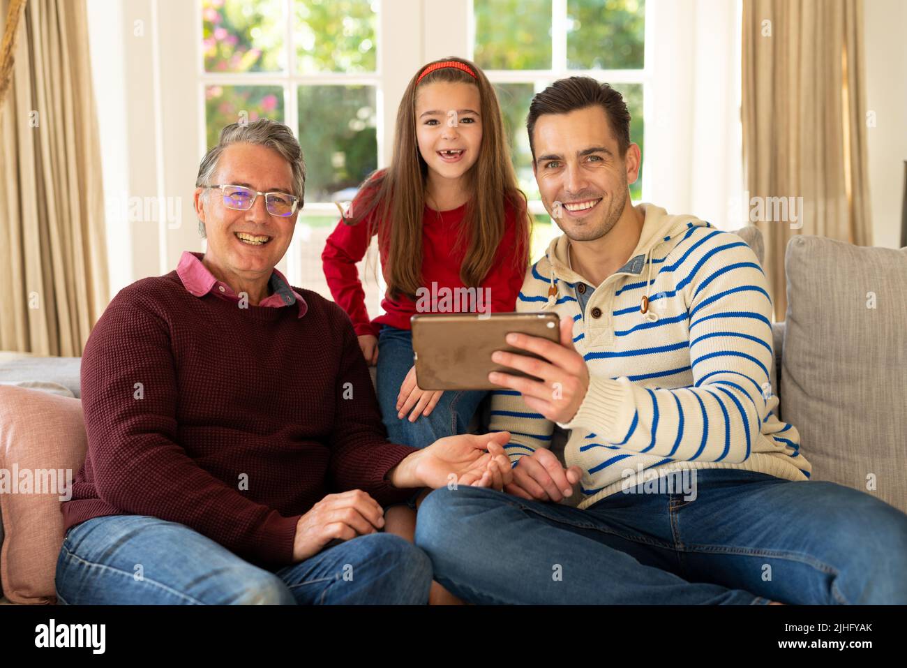 Image de grand-père, père et fille caucasiens heureux assis sur un canapé avec une tablette Banque D'Images