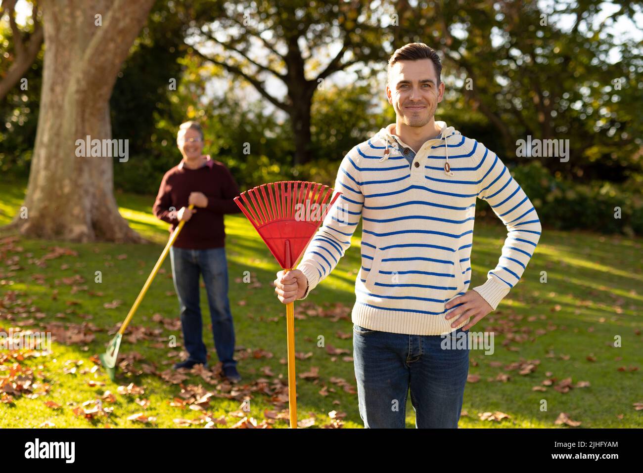 Image d'un père caucasien et d'un fils adulte qui balaie les feuilles dans le jardin Banque D'Images