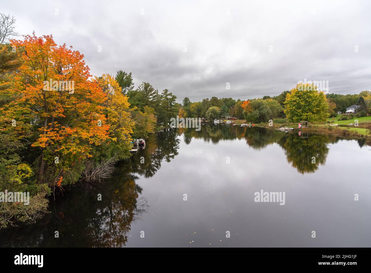 Lac avec côtes boisées sous ciel nuageux en automne. Réflexion dans l'eau. Banque D'Images
