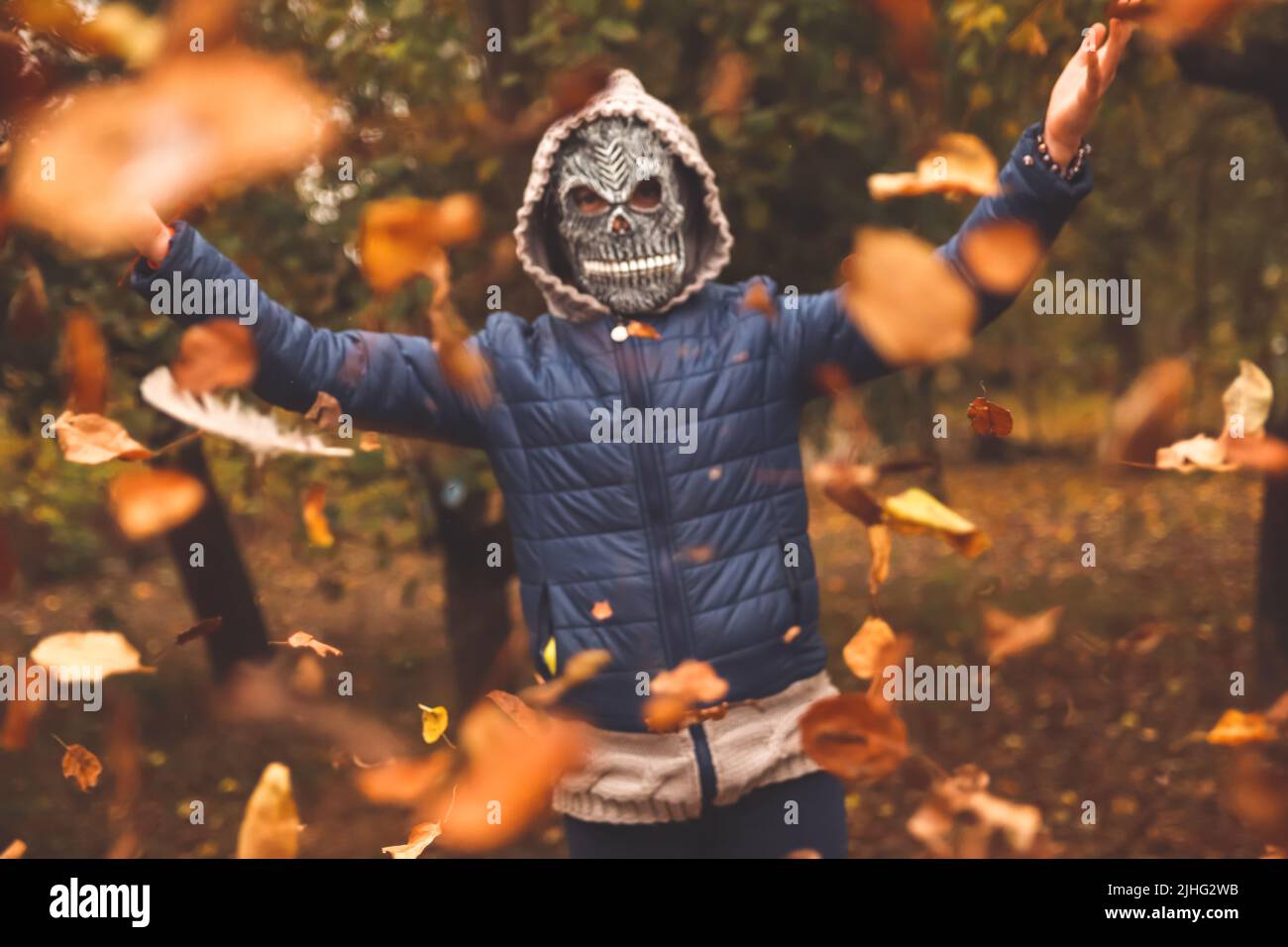 Recentrer les gens d'Halloween. Personne dans le masque de couche sinistre levant la main et jetant les feuilles. De nombreuses feuilles sèches orange, jaune, verte volantes. Copier l'espace. Automne Banque D'Images