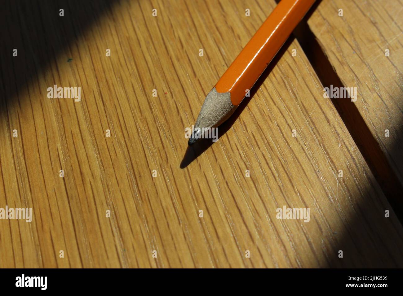 Crayon en bois orange sur fond en bois éclairé par un rayon lumineux Banque D'Images