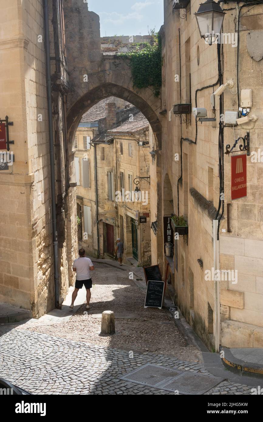 Homme regardant l'ancienne arche connue sous le nom de porte de cadence dans une rue pavée étroite de Saint Emilion France Banque D'Images