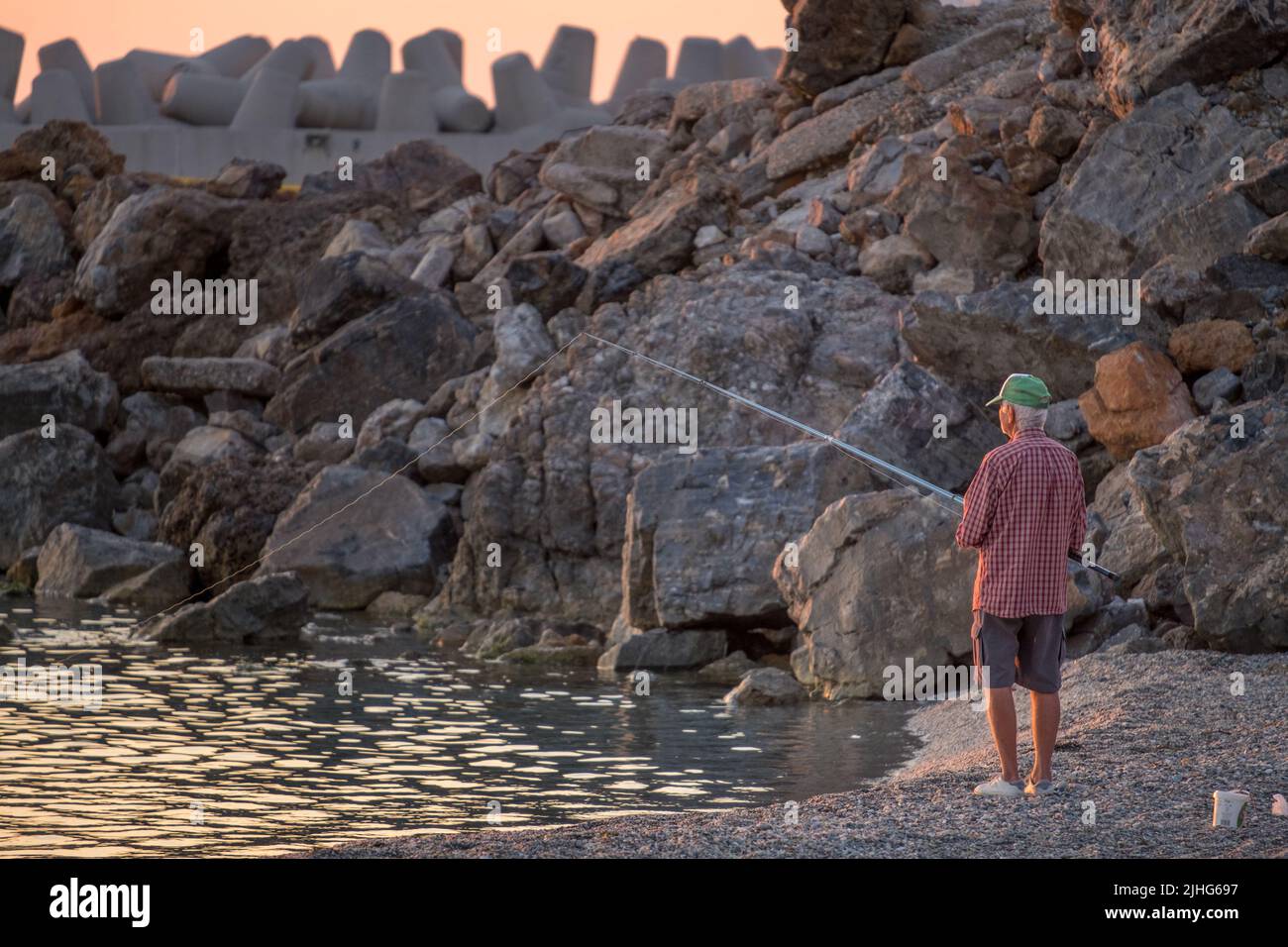 Un vieil homme qui pêche sur la rive, au bord du brise-lames d'un port avec sa canne à pêche Banque D'Images