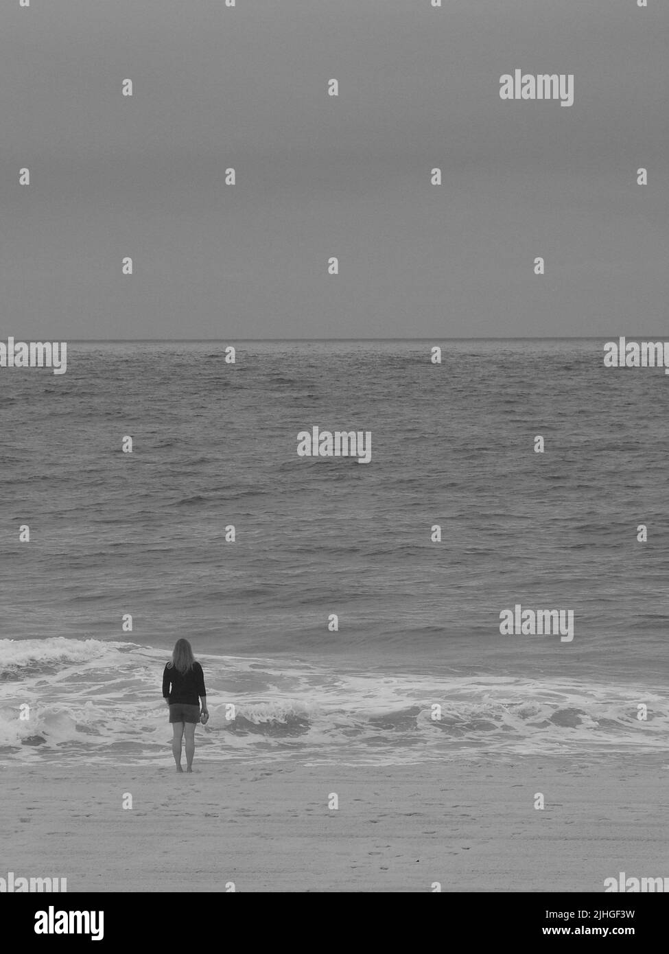 Femme solitaire sur la plage le matin tenant un verre tout en regardant dehors à la mer. Banque D'Images