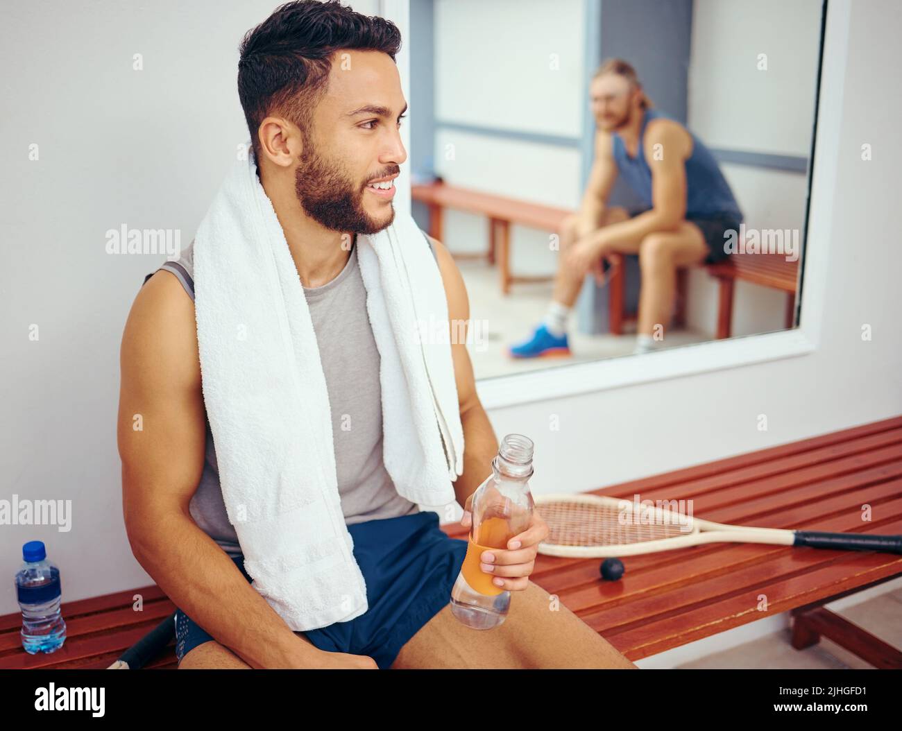 Un jeune joueur boit de l'eau tout en parlant à son ami. Deux amis se sont encolés après un match de squash. Deux hommes assis dans un vestiaire de salle de gym après un match Banque D'Images