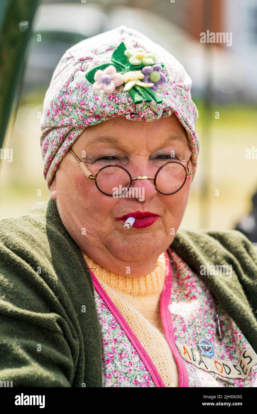 Portrait de la tête et de l'épaule d'une femme âgée vêtue de vêtements de classe ouvrière des années 1940. Cockney typique avec foulard, lunettes et cigarettes à fumer Banque D'Images