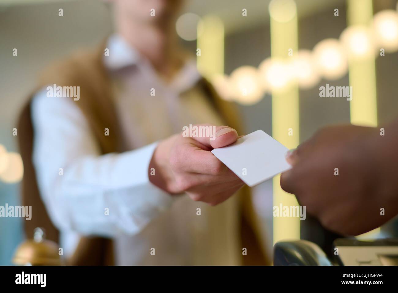 Main d'un jeune homme de travail ou invité de l'hôtel prenant la carte-clé tenue par une réceptionniste afro-américaine après l'inscription Banque D'Images