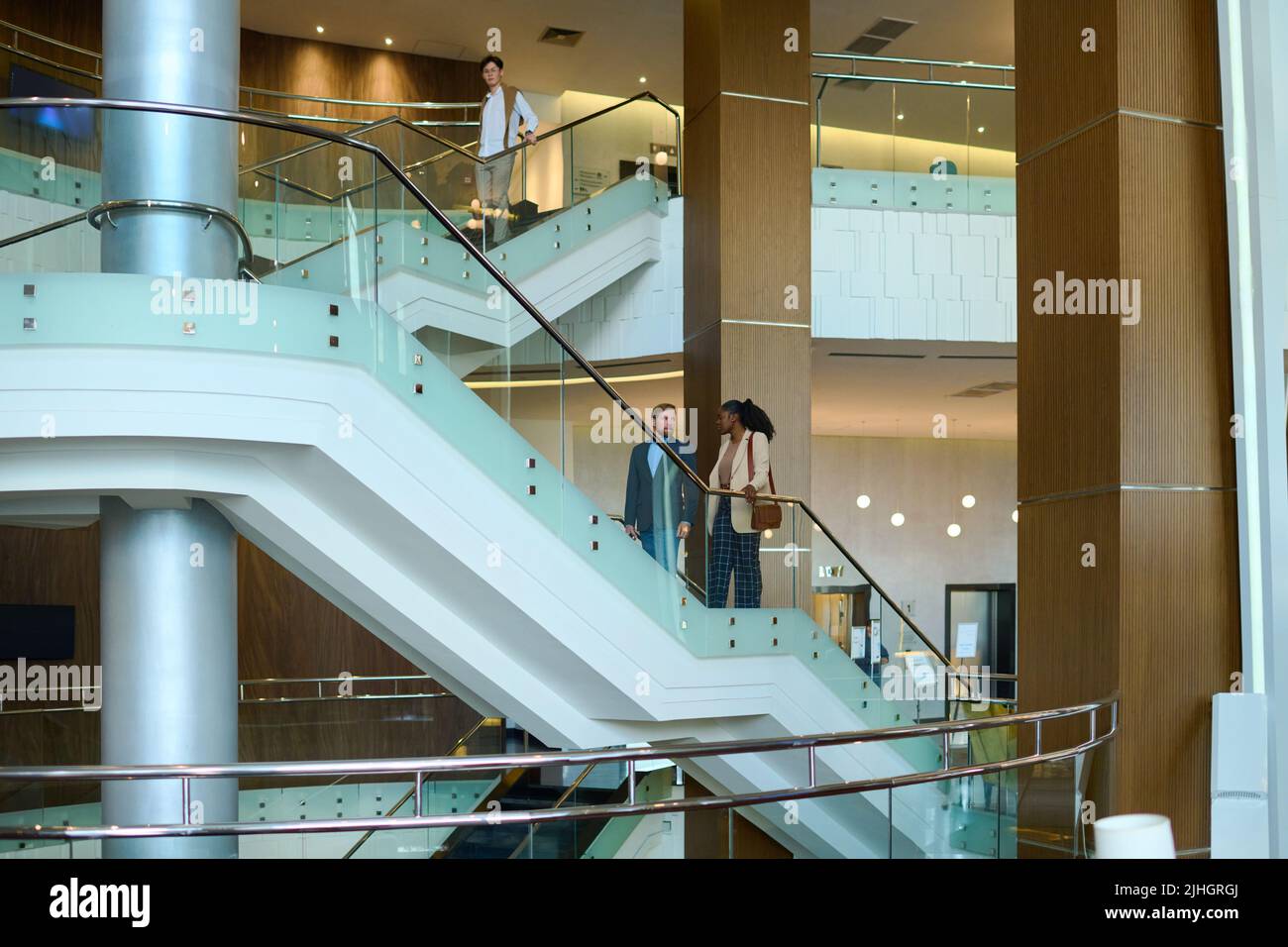 Deux jeunes collègues multiculturels en tenue de cérémonie qui parlent tout en se déplaçant à l'étage sur l'escalier dans le salon de l'hôtel pendant les voyages d'affaires Banque D'Images