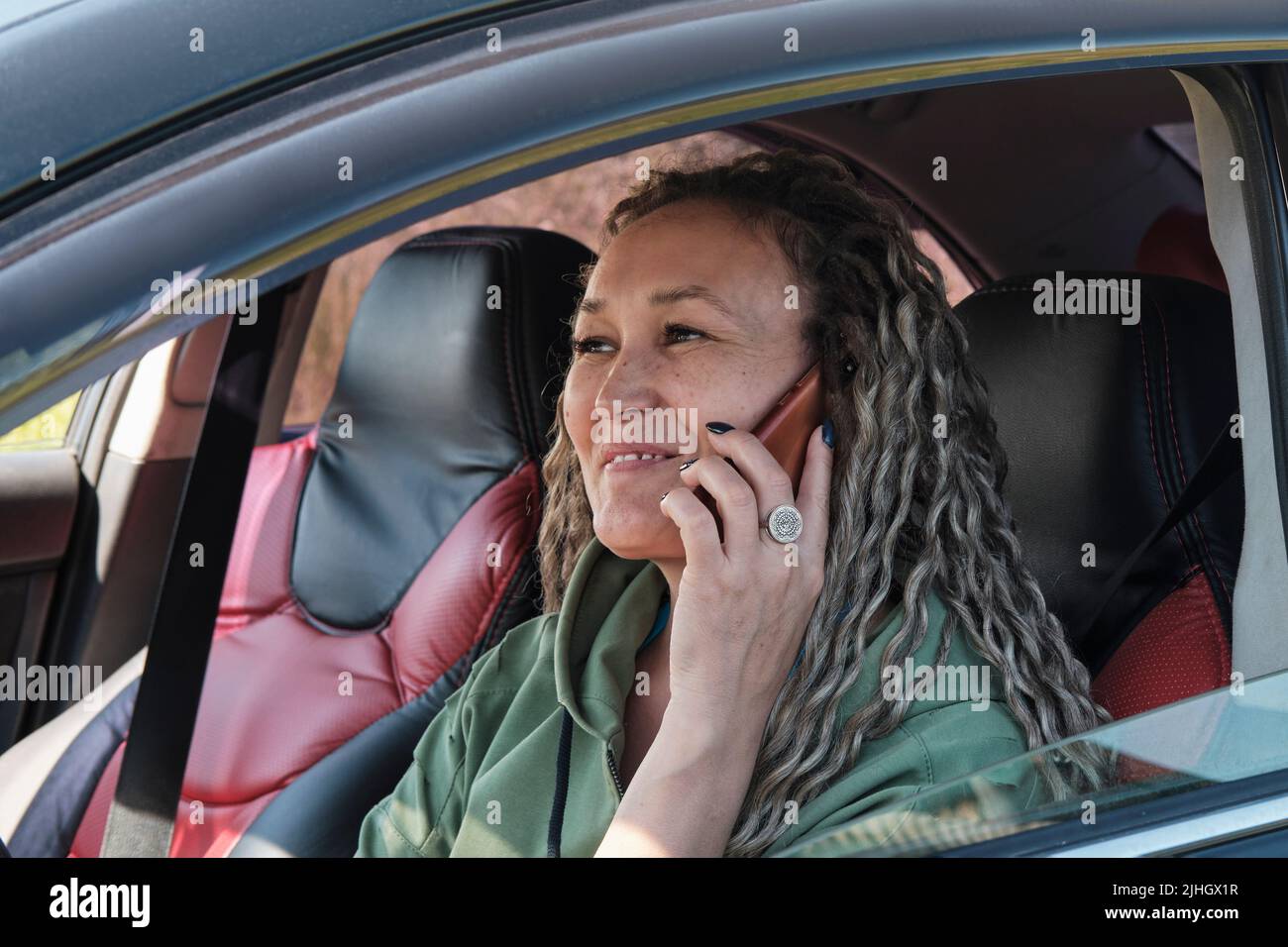 Une jolie femme asiatique d'âge moyen souriante assise dans une voiture parlant au téléphone. Banque D'Images