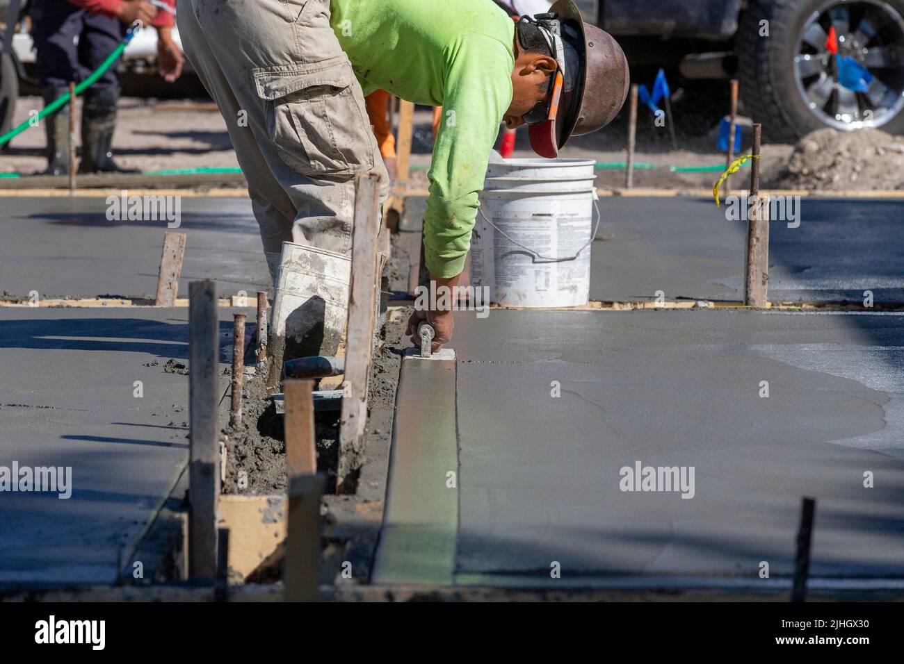 Un ouvrier de la construction utilise une truelle de virage pour terminer le bord d'une gifle de béton fraîchement versée comme une allée. Banque D'Images