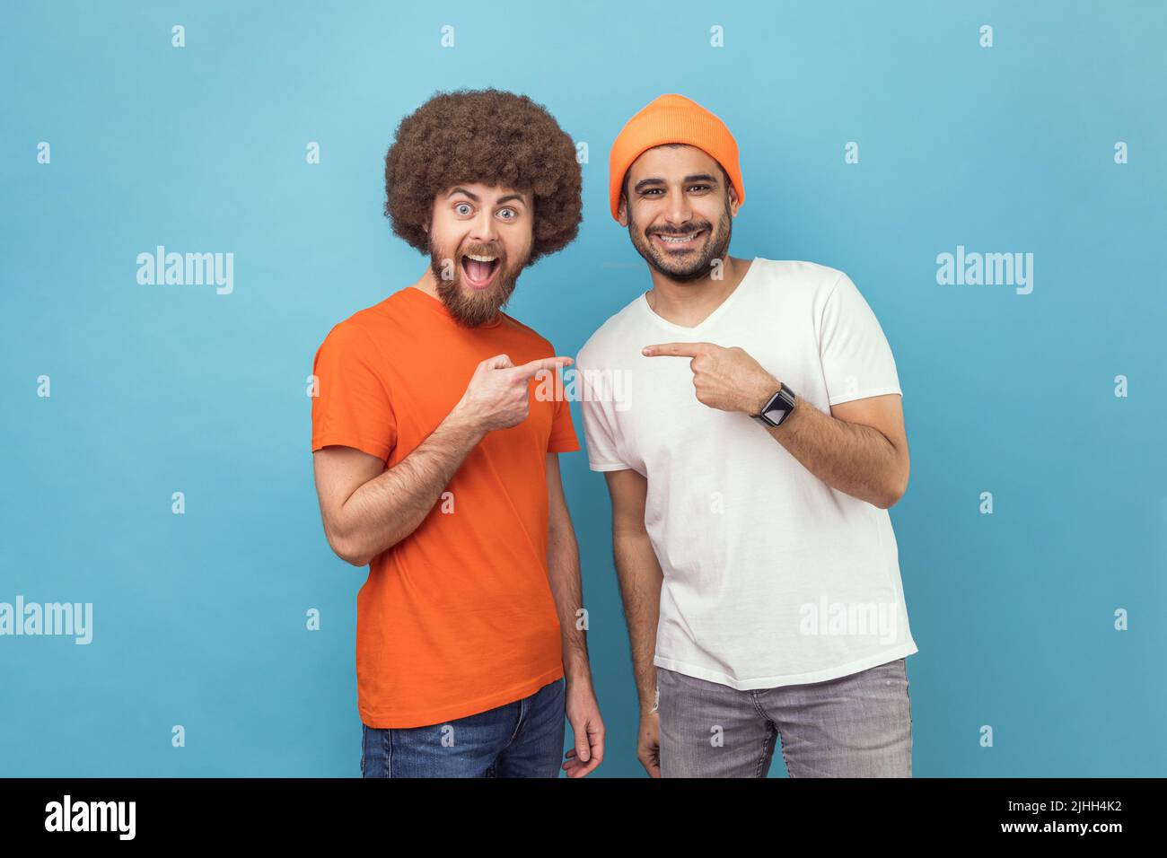 Meilleurs amis. Portrait de deux jeunes adultes hipster hommes pointant du doigt l'un vers l'autre et regardant la caméra avec des expressions positives joyeuses. Studio d'intérieur isolé sur fond bleu. Banque D'Images Meilleurs amis. Portrait de deux jeunes adultes hipster hommes pointant du doigt l'un vers l'autre et regardant la caméra avec des expressions positives joyeuses. Studio d'intérieur isolé sur fond bleu. Banque D'Images