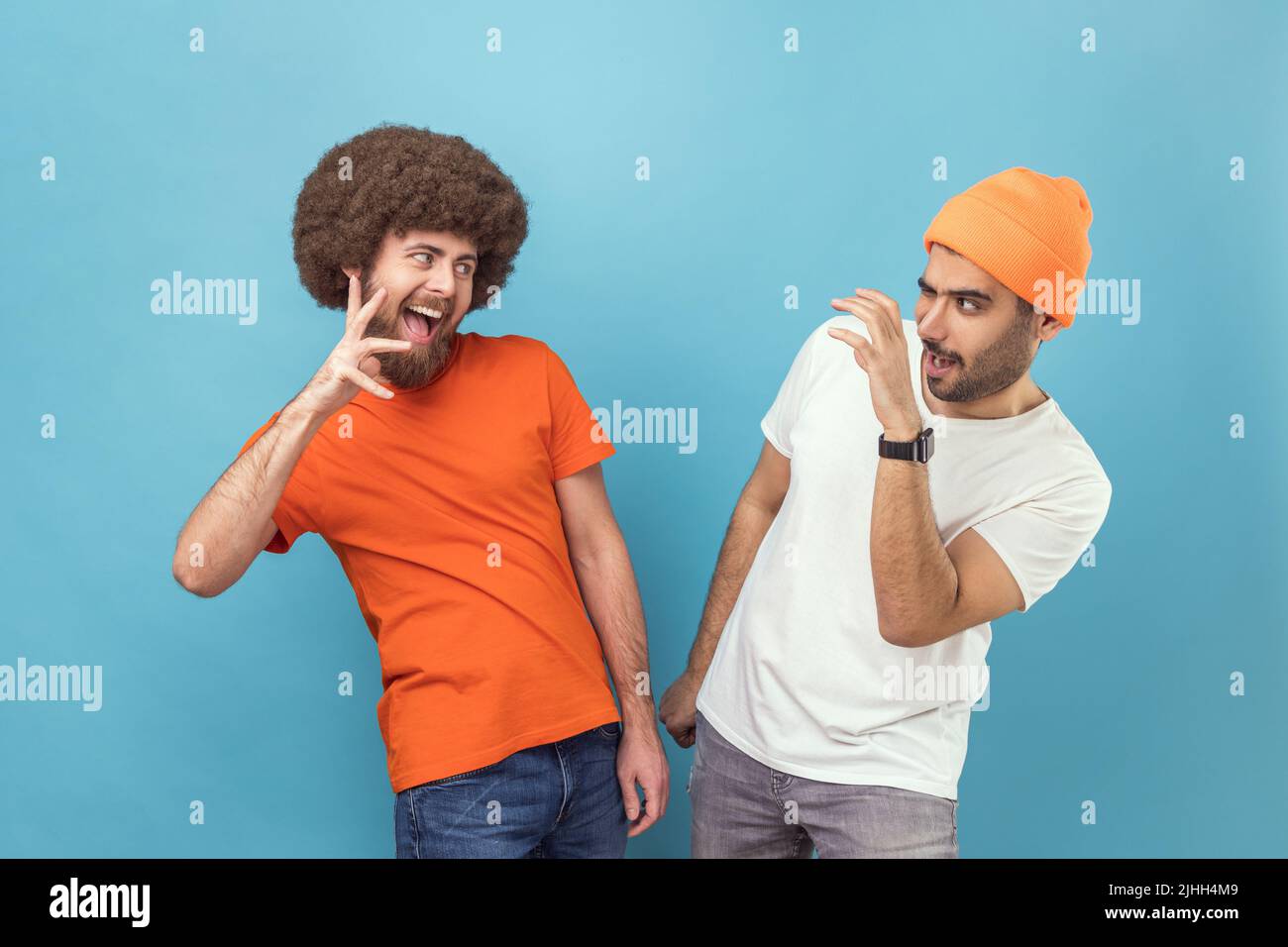 Portrait de deux jeunes adultes fous hipster hommes en T-shirts debout avec des griffes levées, regardant l'un l'autre avec l'expression faciale drôle. Studio d'intérieur isolé sur fond bleu. Banque D'Images Portrait de deux jeunes adultes fous hipster hommes en T-shirts debout avec des griffes levées, regardant l'un l'autre avec l'expression faciale drôle. Studio d'intérieur isolé sur fond bleu. Banque D'Images