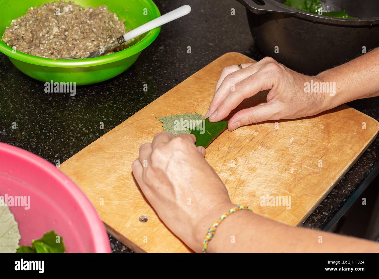 Une femme prépare de la nourriture à la maison. La viande hachée est enveloppée dans des feuilles de raisin sur une planche de bois, le dolma. Banque D'Images