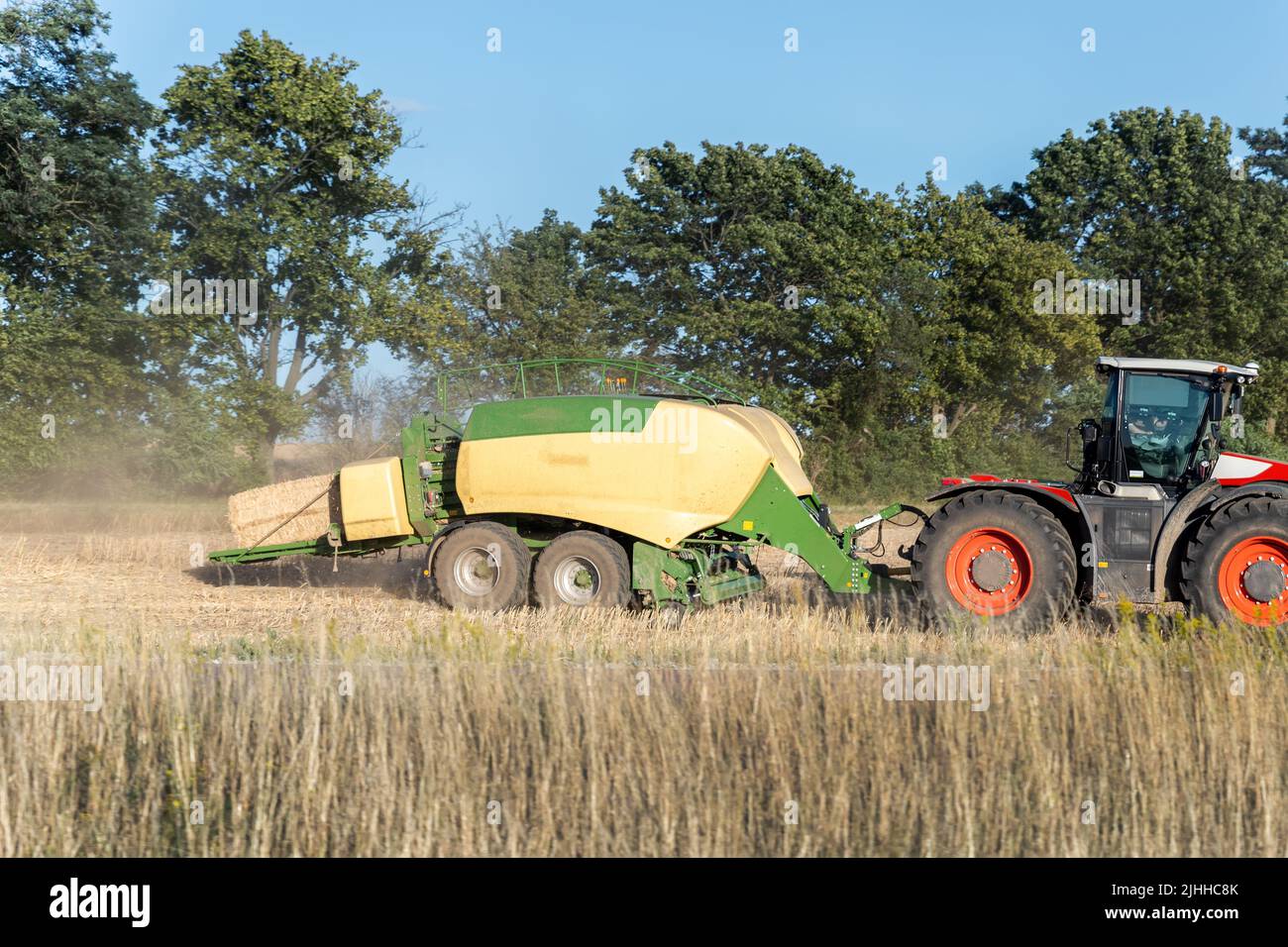 Vue latérale d'un grand tracteur moderne avec remorque de la presse à balles pour la fabrication de blocs de fourrage après la récolte du blé dans les champs. Équipement agricole et répartition Banque D'Images