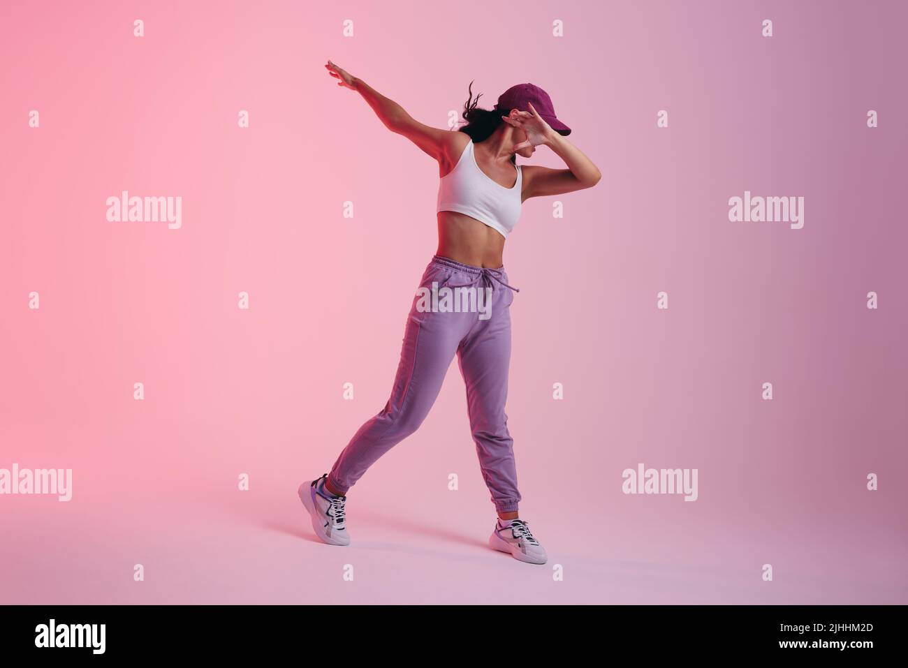 Jeune femme qui fait le mouvement de danse dab en se tenant dans un studio. Jeune femme active dansant dans les vêtements de sport. Banque D'Images