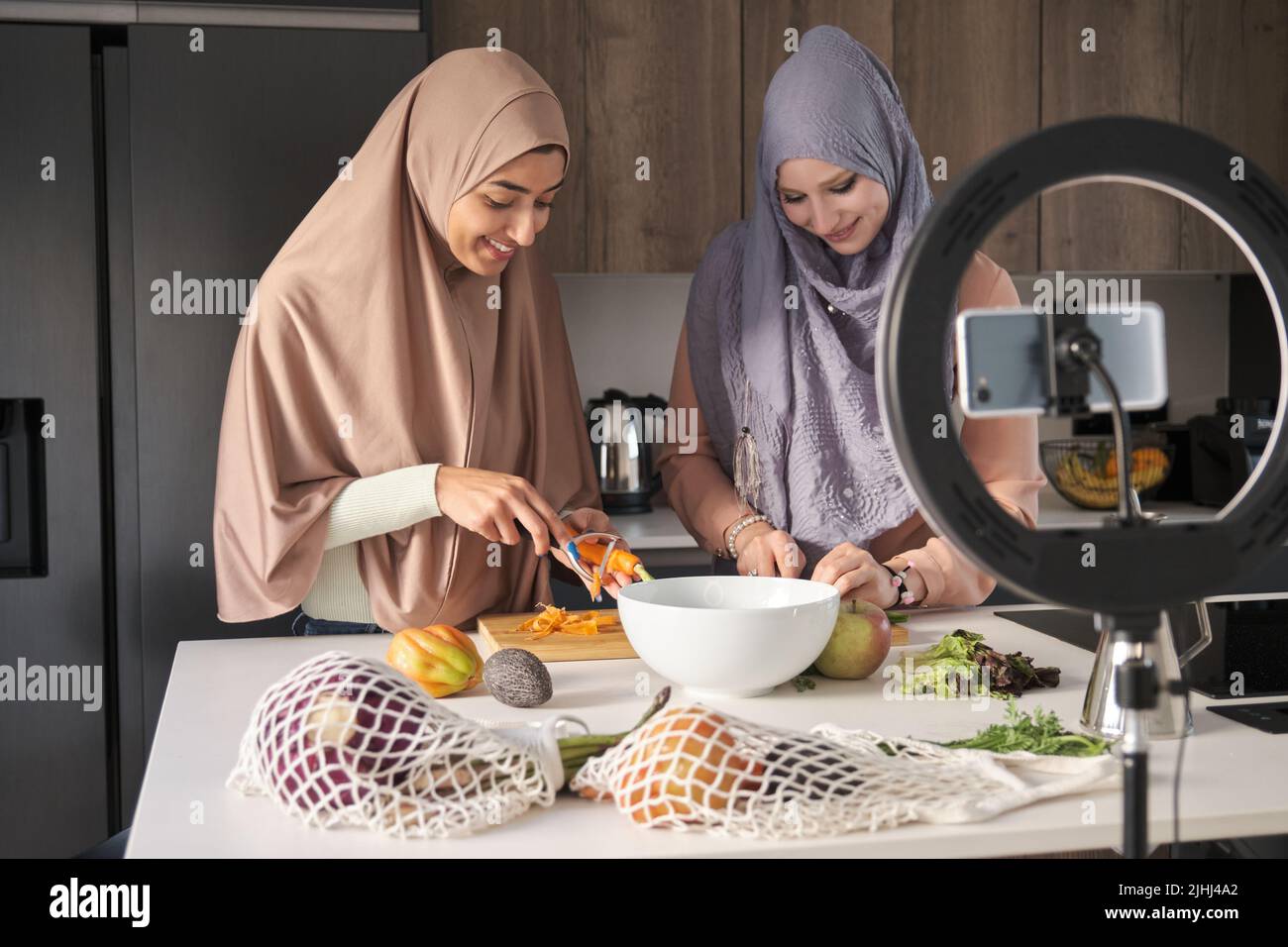 Deux influenceurs musulmans tranchant, hachant et épluchant des légumes dans la cuisine. Banque D'Images
