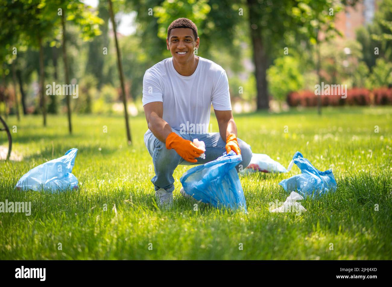 Un gars souriant à l'appareil photo ramassant les déchets de l'herbe Banque D'Images