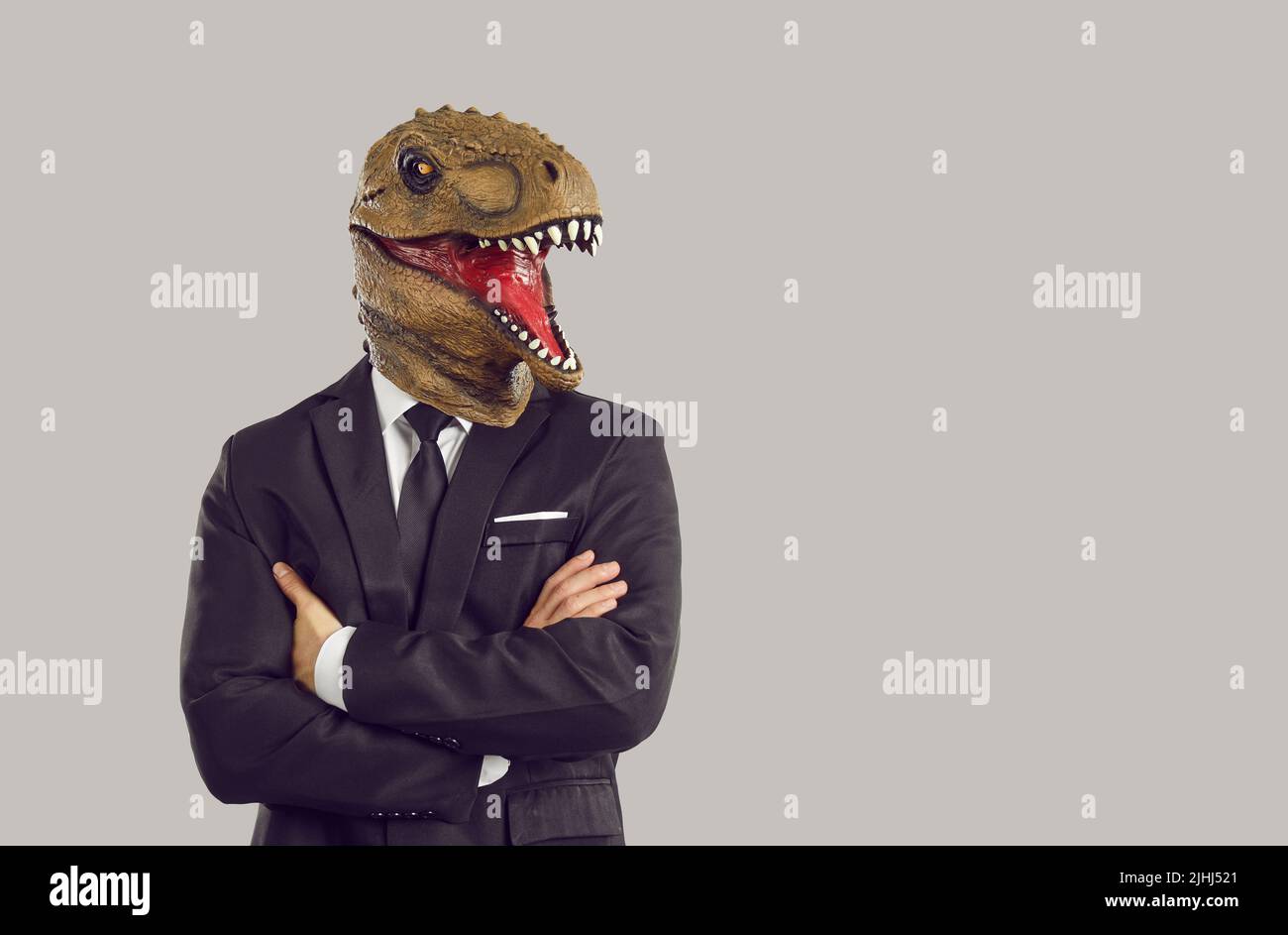 Homme drôle avec masque de dinosaure sur les supports de tête en studio avec les bras croisés vêtu d'un costume d'affaires Banque D'Images