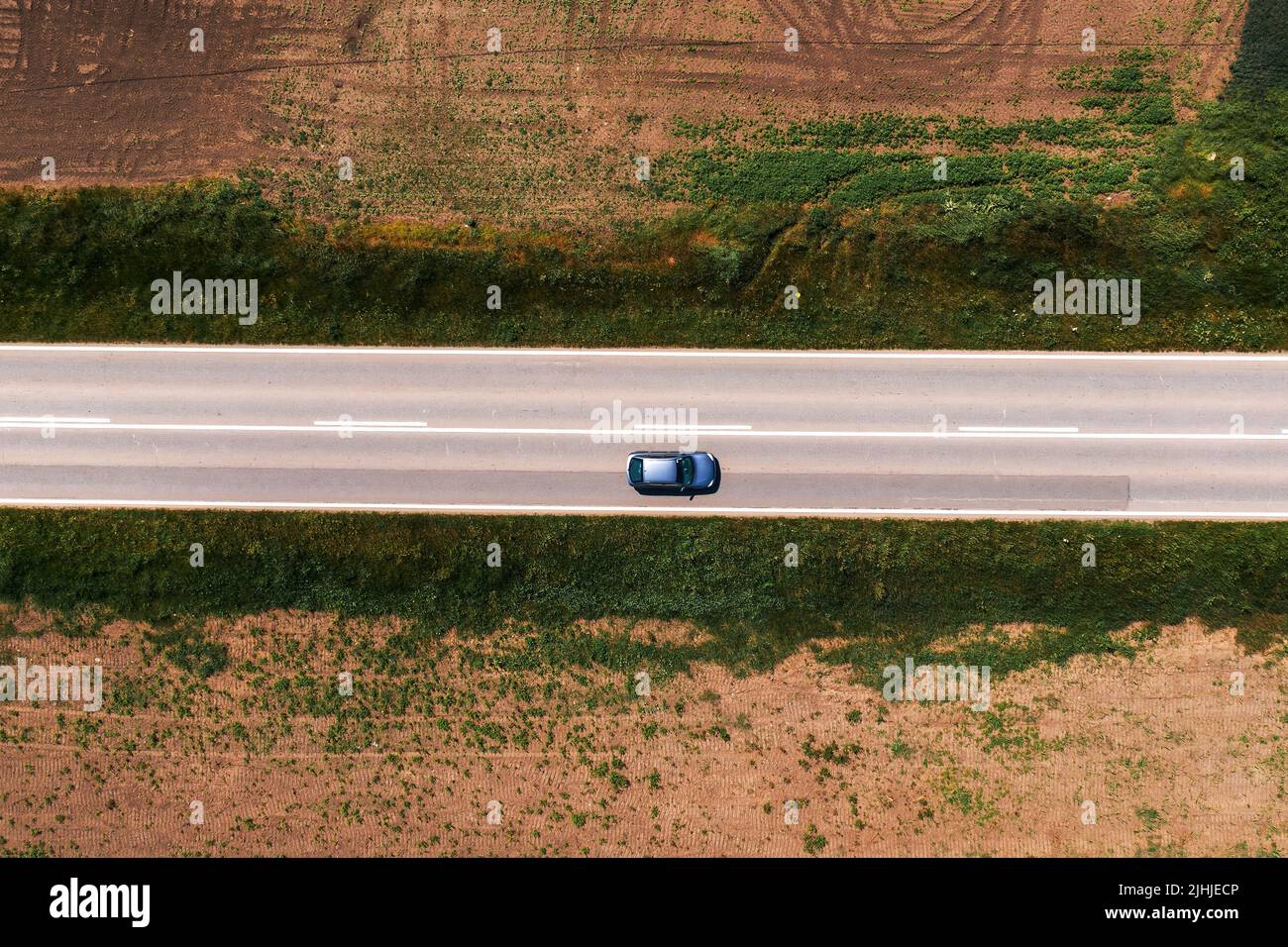 Photo aérienne de voiture de tourisme conduite le long de la route asphaltée à travers le paysage de campagne sans arbres et de l'ombre sur chaud ensoleillé l'après-midi d'été, drone pov Banque D'Images
