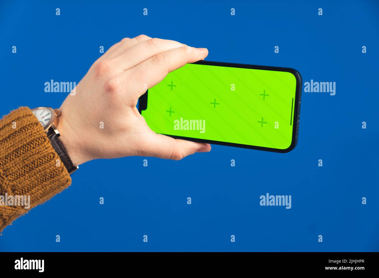 Main tenant le smartphone avec la touche verte de couleur d'écran verticalement sur l'arrière-plan bleu de l'écran. Photo de haute qualité Banque D'Images