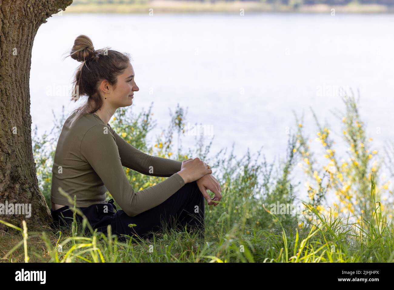 La jeune femme brune, assise dans une forêt verte, jouit du silence et de la beauté de la nature en regardant au-dessus d'un lac de la forêt bleue par une journée d'été. Photo de haute qualité Banque D'Images
