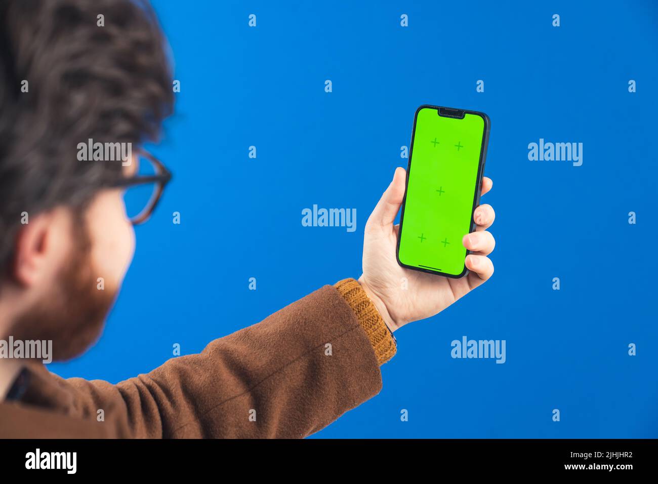 Homme tenant le smartphone avec la touche verte de couleur d'écran avec les traqueurs sur l'arrière-plan bleu de l'écran. Photo de haute qualité Banque D'Images