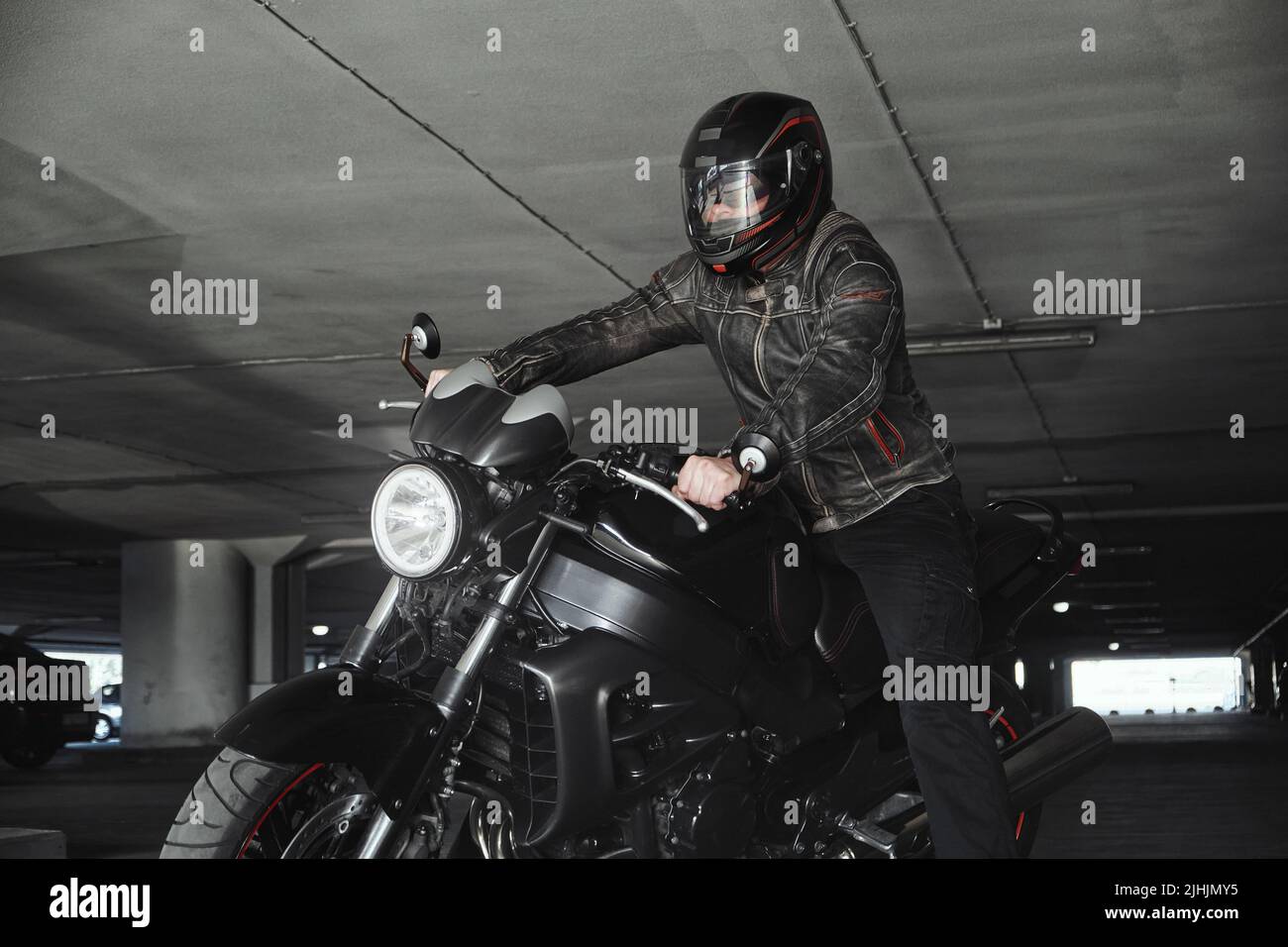 Un homme dans un casque assis sur une moto dans un garage souterrain Banque D'Images