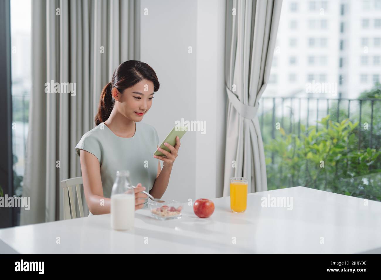 une femme asiatique mange un déjeuner avec son téléphone entre ses mains Banque D'Images