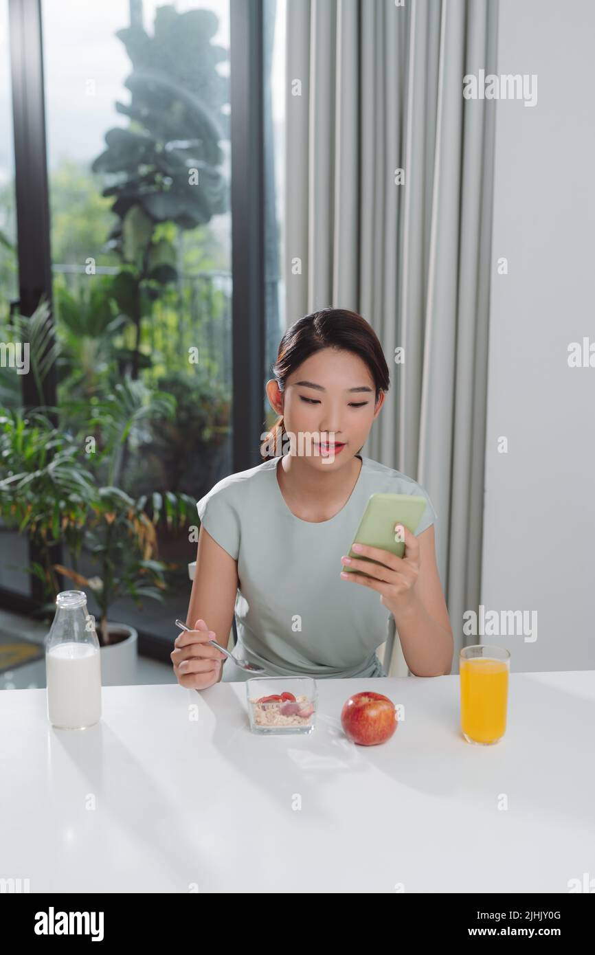 une femme asiatique mange un déjeuner avec son téléphone entre ses mains Banque D'Images