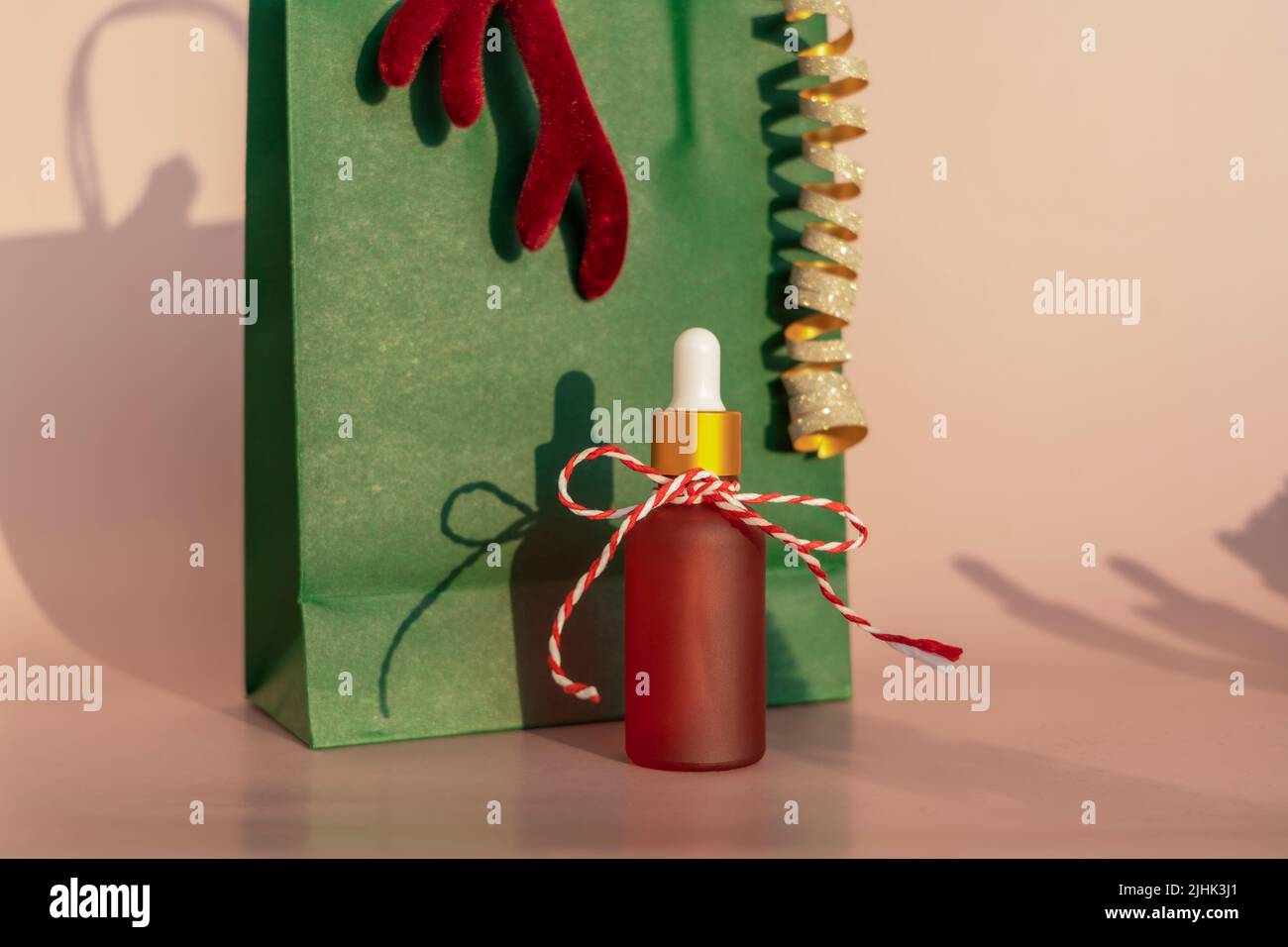 Un flacon compte-gouttes d'huile essentielle naturelle ou de sérum sur fond rose comme cadeau pour les vacances de Noël Banque D'Images