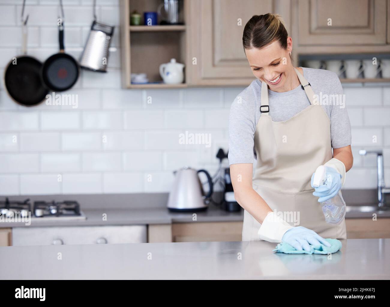 Les surfaces brillantes sont si satisfaisantes. Une jeune femme essuyant une surface de cuisine avec un détergent et un chiffon à la maison. Banque D'Images