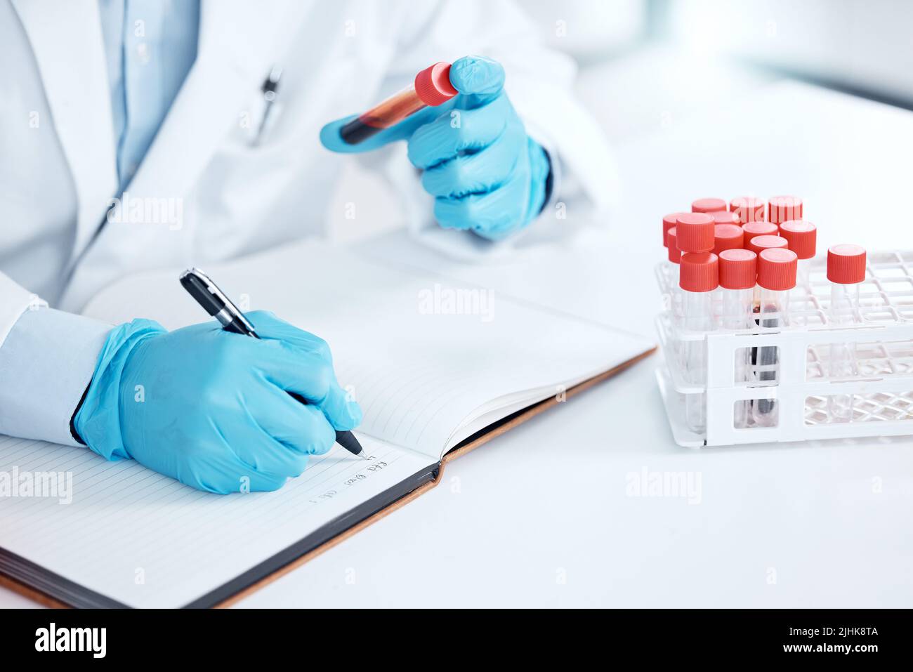 Mains d'un scientifique écrivant des notes sur un échantillon de recherche, tenant un tube à essai. Un scientifique travaillant sur une expérience de chimie tient un flacon de sang Banque D'Images