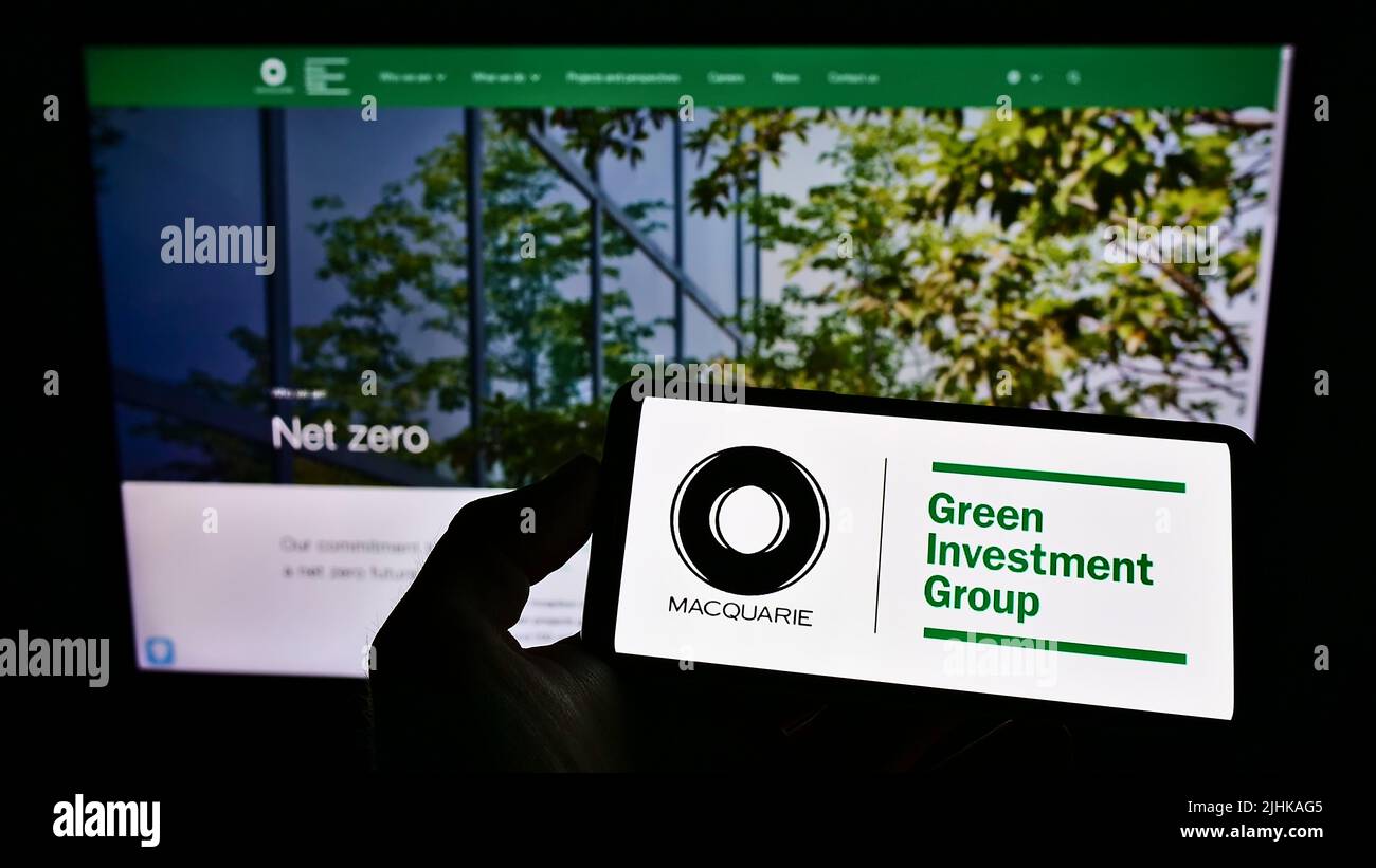 Personne tenant un téléphone portable avec le logo de la société Green Investment Group Limited (GIG) sur l'écran en face de la page Web. Mise au point sur l'affichage du téléphone. Banque D'Images