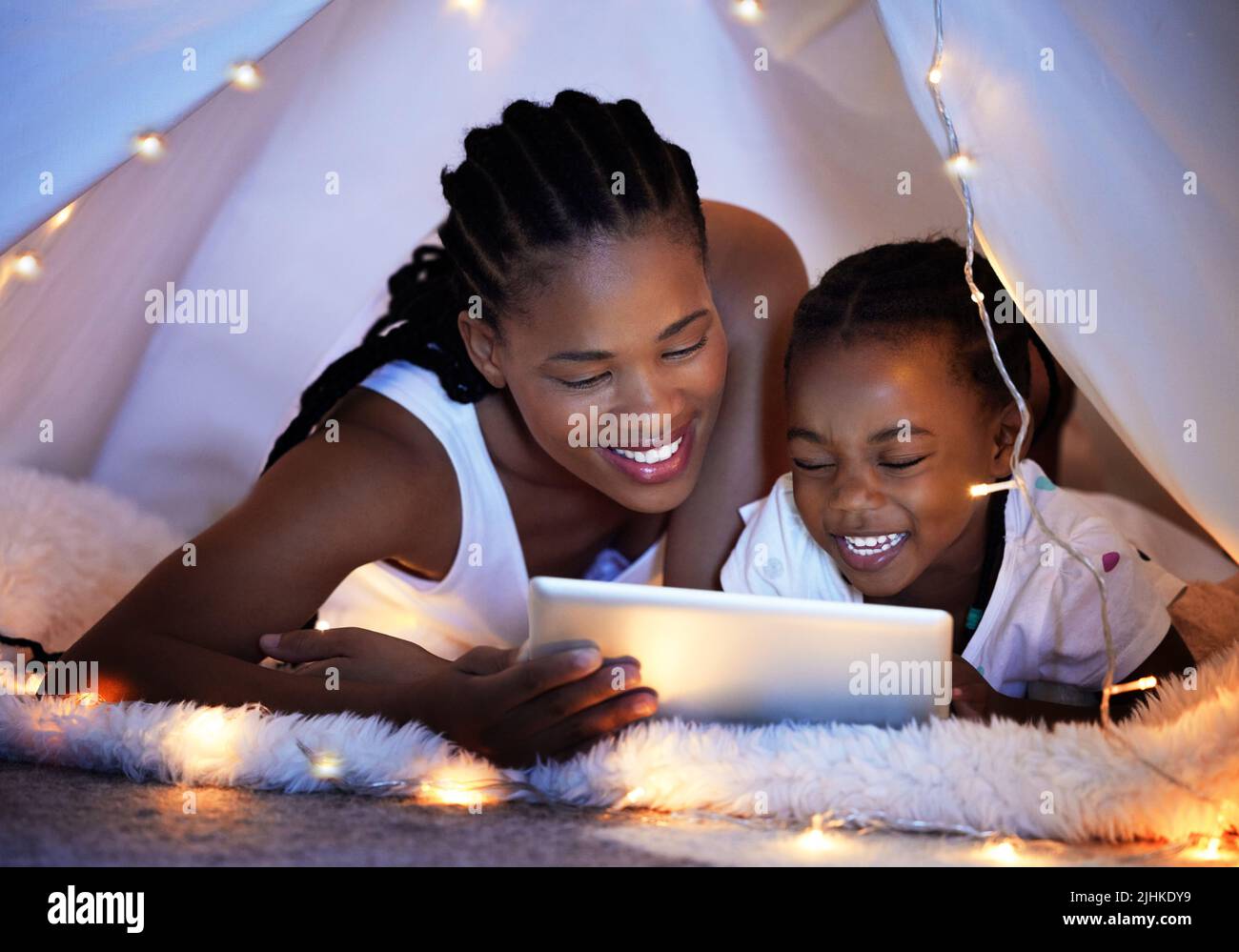 C'est leur tradition de lire les histoires de coucher ensemble. Une mère et sa fille utilisant une tablette numérique ensemble tout en se relaxant sous une couverture fort à Banque D'Images