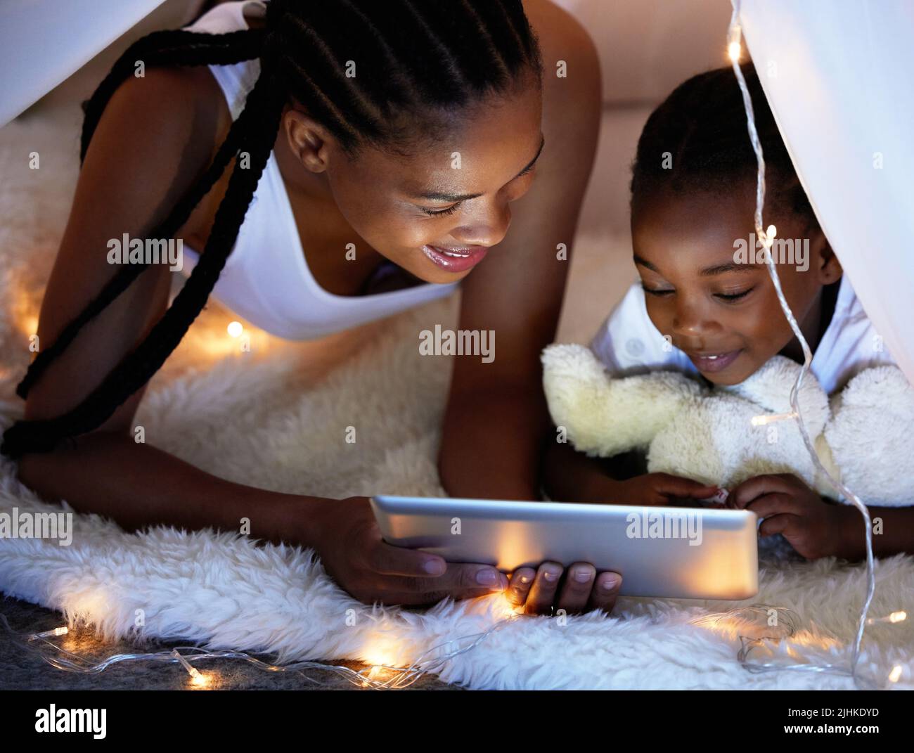 Il y a tellement de choses à voir et à apprendre en ligne. Une mère et sa fille utilisent une tablette numérique ensemble tout en se détendant sous une couverture fort à la maison. Banque D'Images