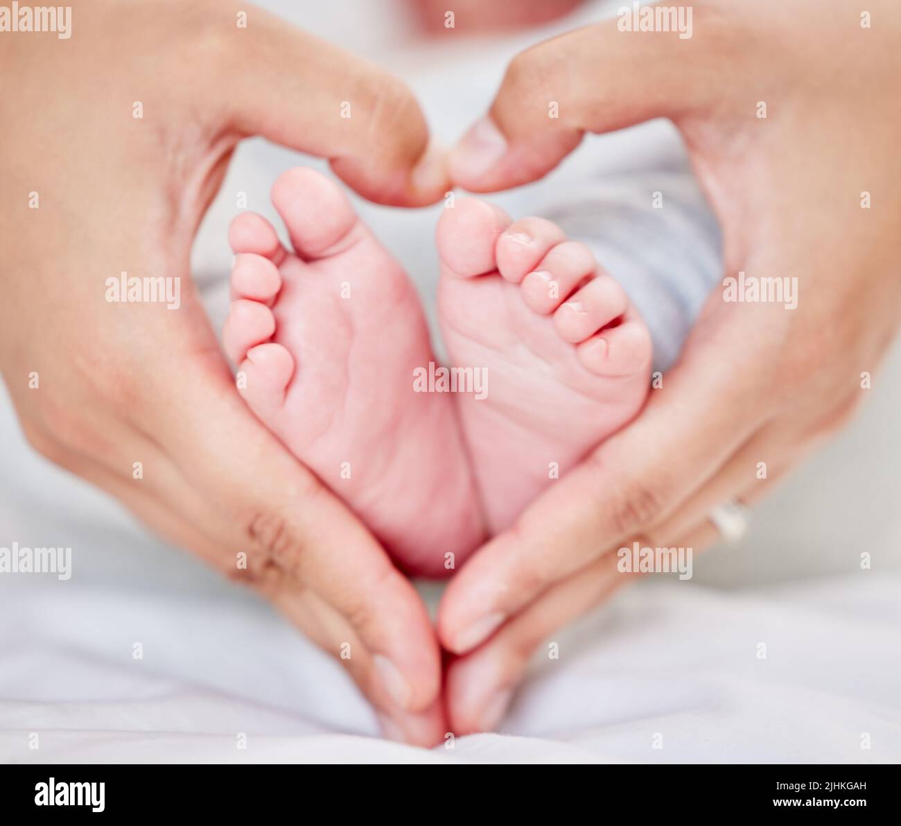 Gros plan des mains d'un parent formant une forme de coeur autour des petits pieds de bébé nouveau-né. Mère aimant son petit bébé. Petit bébé qui se repose dans sa chambre de bébé Banque D'Images