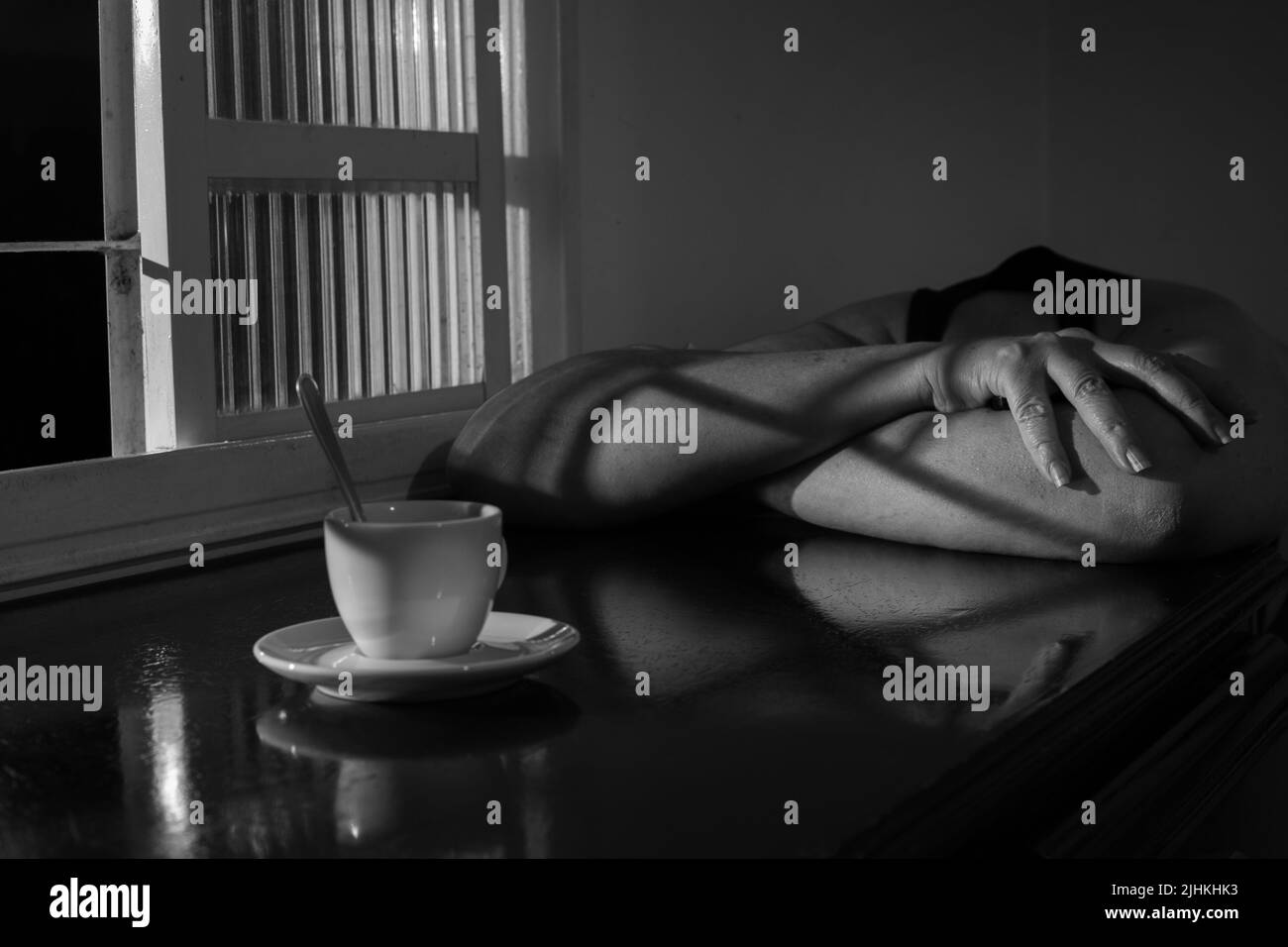 Goiania, Goiás, Brésil – 18 juillet 2022: Une personne avec sa tête vers le bas et s'appuyant sur une table avec une tasse de café, à côté d'une fenêtre. Banque D'Images