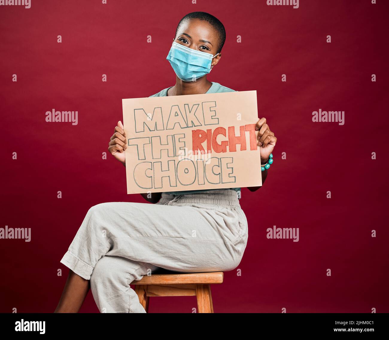 Femme vaccinée Covid afro-américaine montrant, tenant une affiche et portant un masque chirurgical. Happy Black model isolé sur fond rouge studio Banque D'Images
